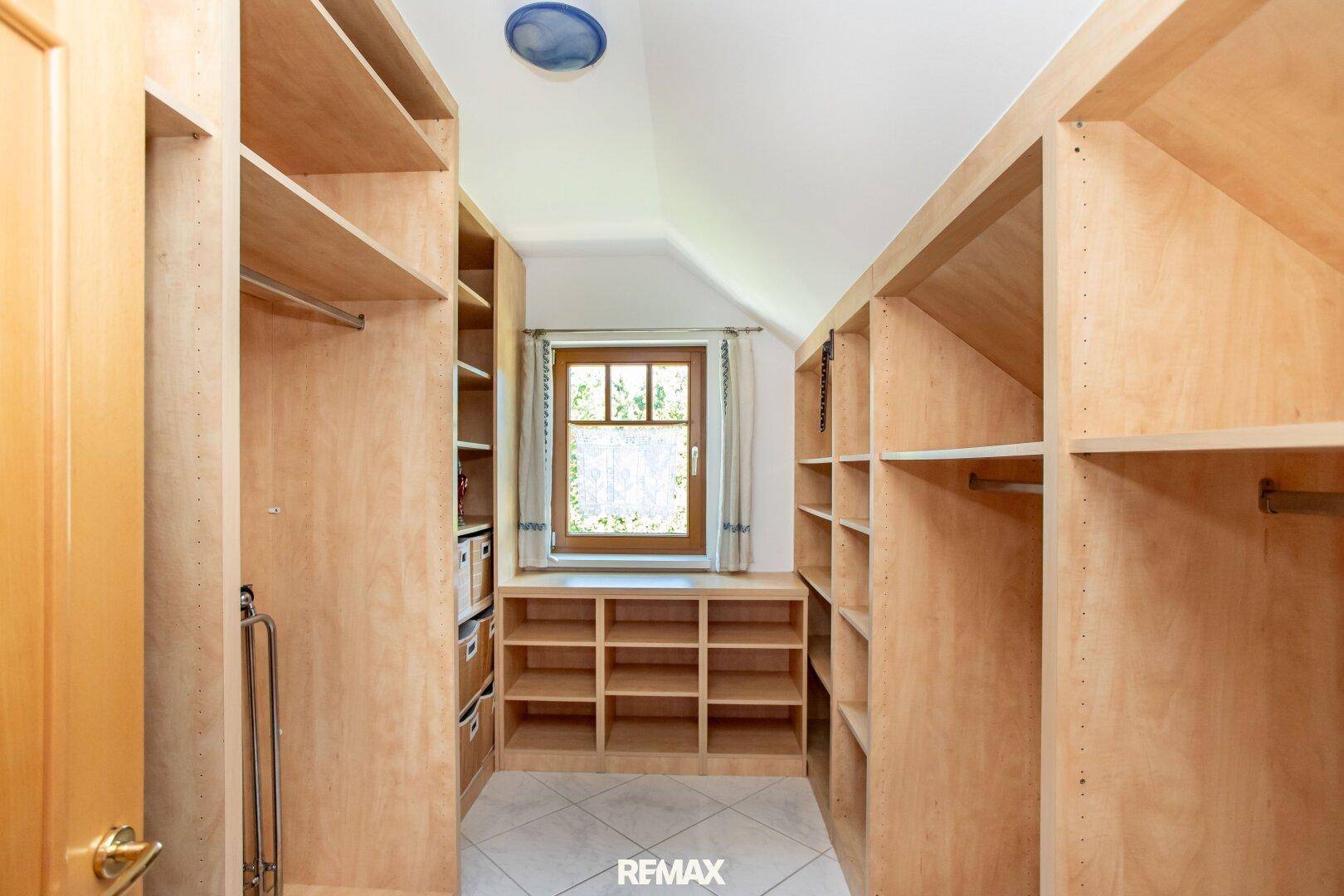 Geräumiges Ankleidezimmer mit maßgefertigten Holzregalen und Fenster für Tageslicht.