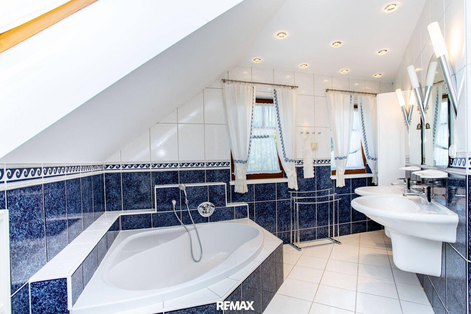 Großes Badezimmer im Dachgeschoss mit Eckbadewanne, Doppelwaschbecken und blauen Fliesen.