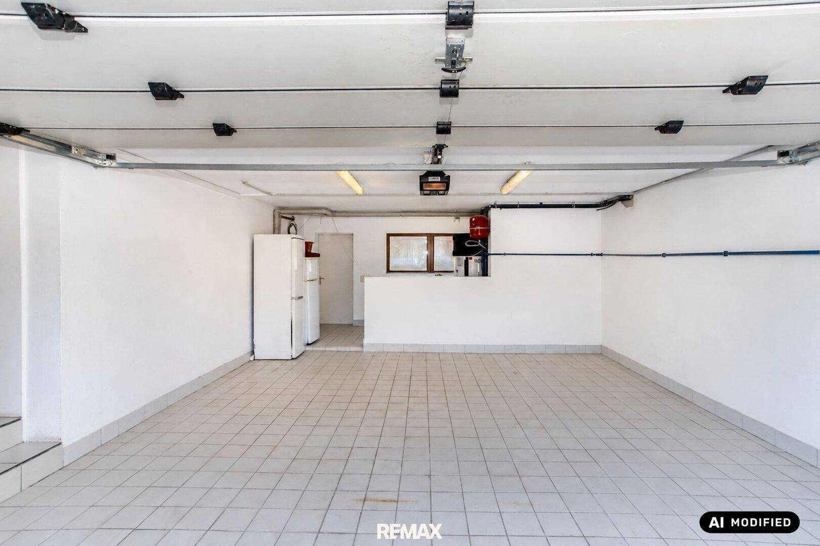 Leere Garage mit Fliesenboden, weiß gestrichenen Wänden und Stauraum im hinteren Bereich.