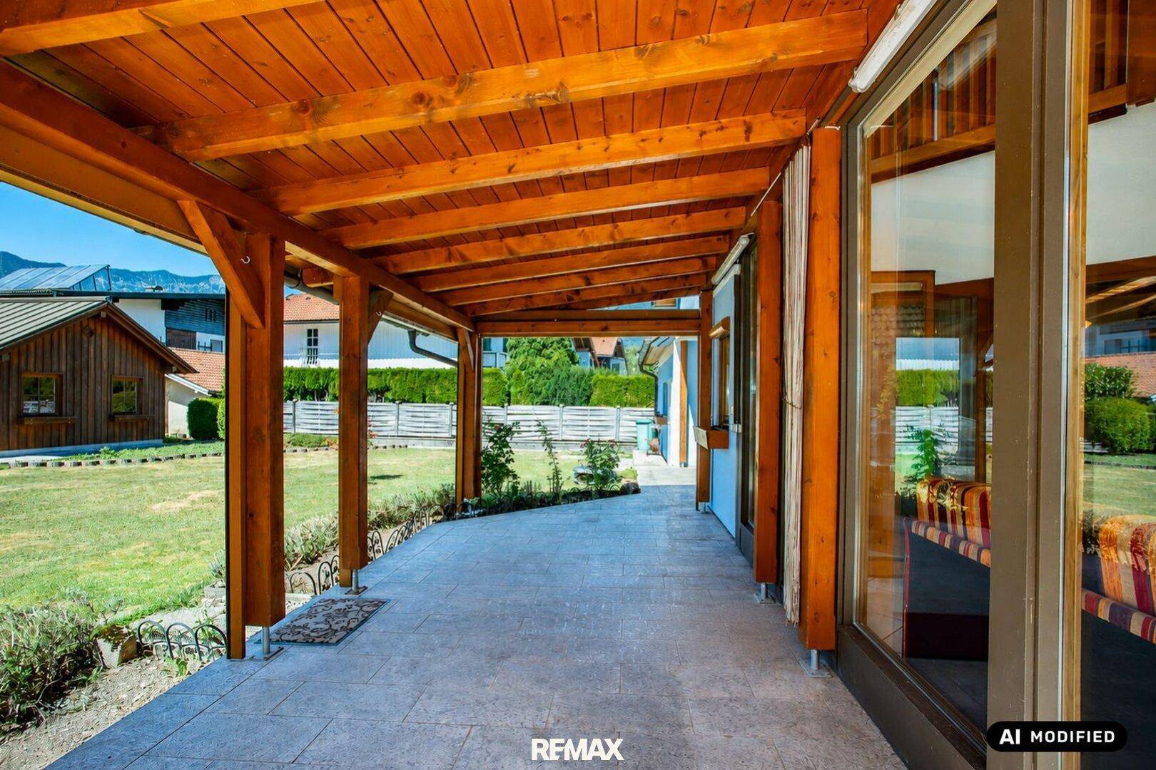 Überdachte Terrasse mit Holzbalken, Fliesenboden und Blick in den grünen Garten.