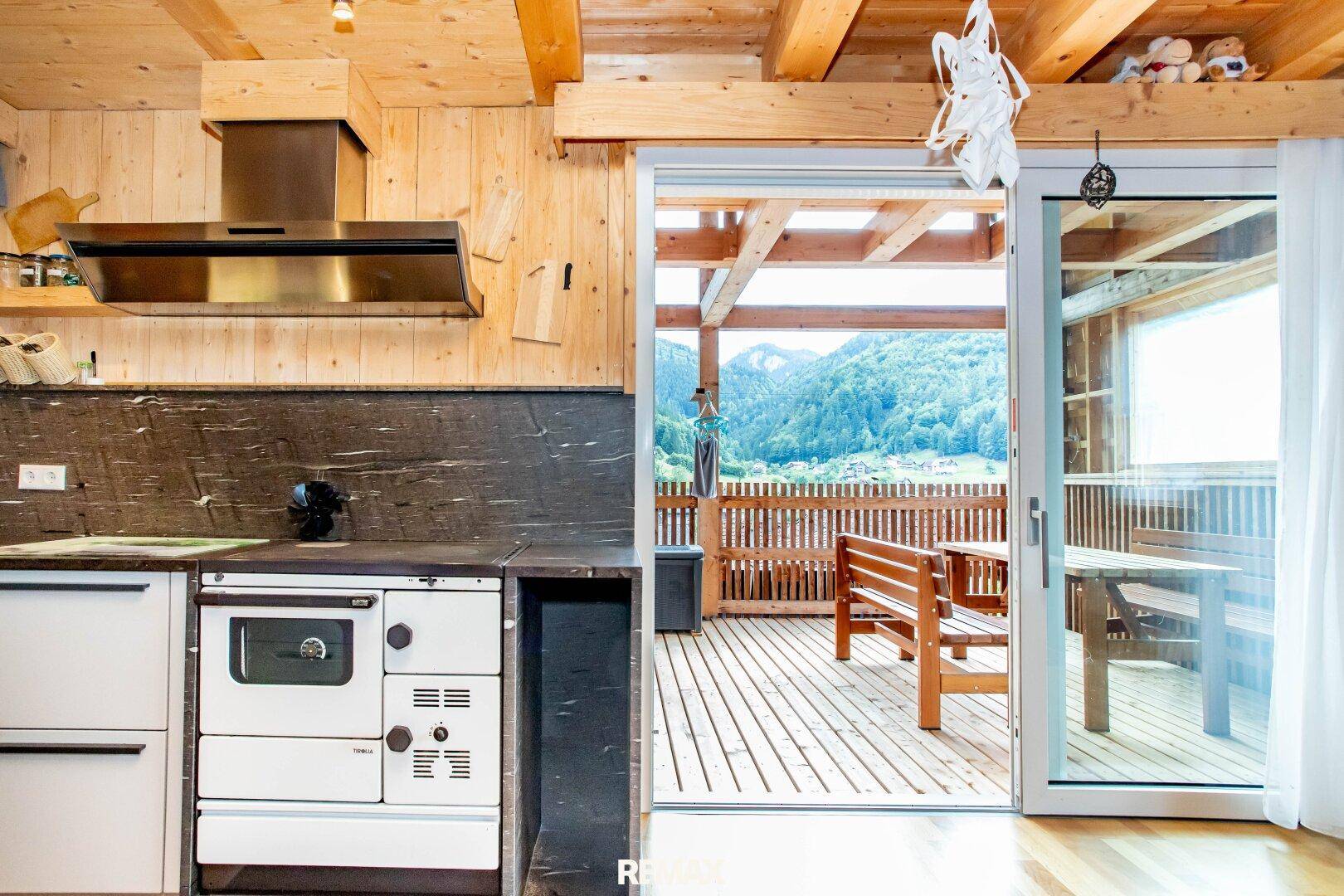Küche mit traditionellem Holzofen und Schiebetür, die zu einer Terrasse mit Bergblick führt.