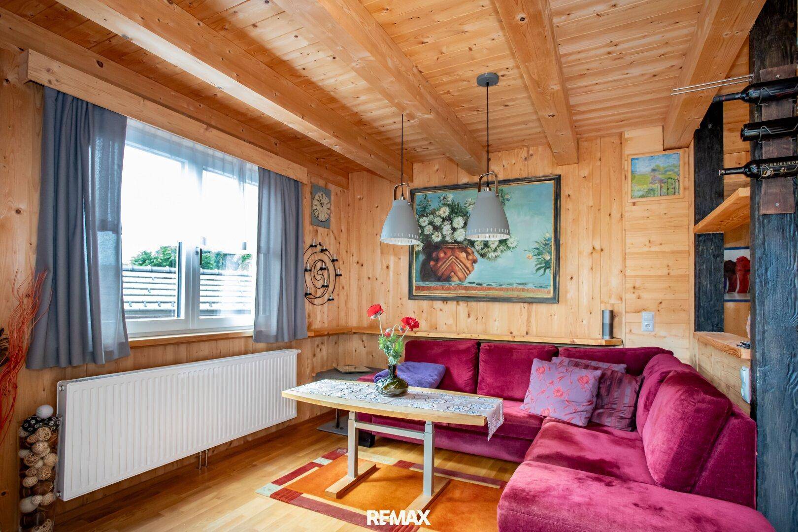 Gemütliches Wohnzimmer mit Holzvertäfelung, rotem Sofa und Blick auf die grüne Umgebung.