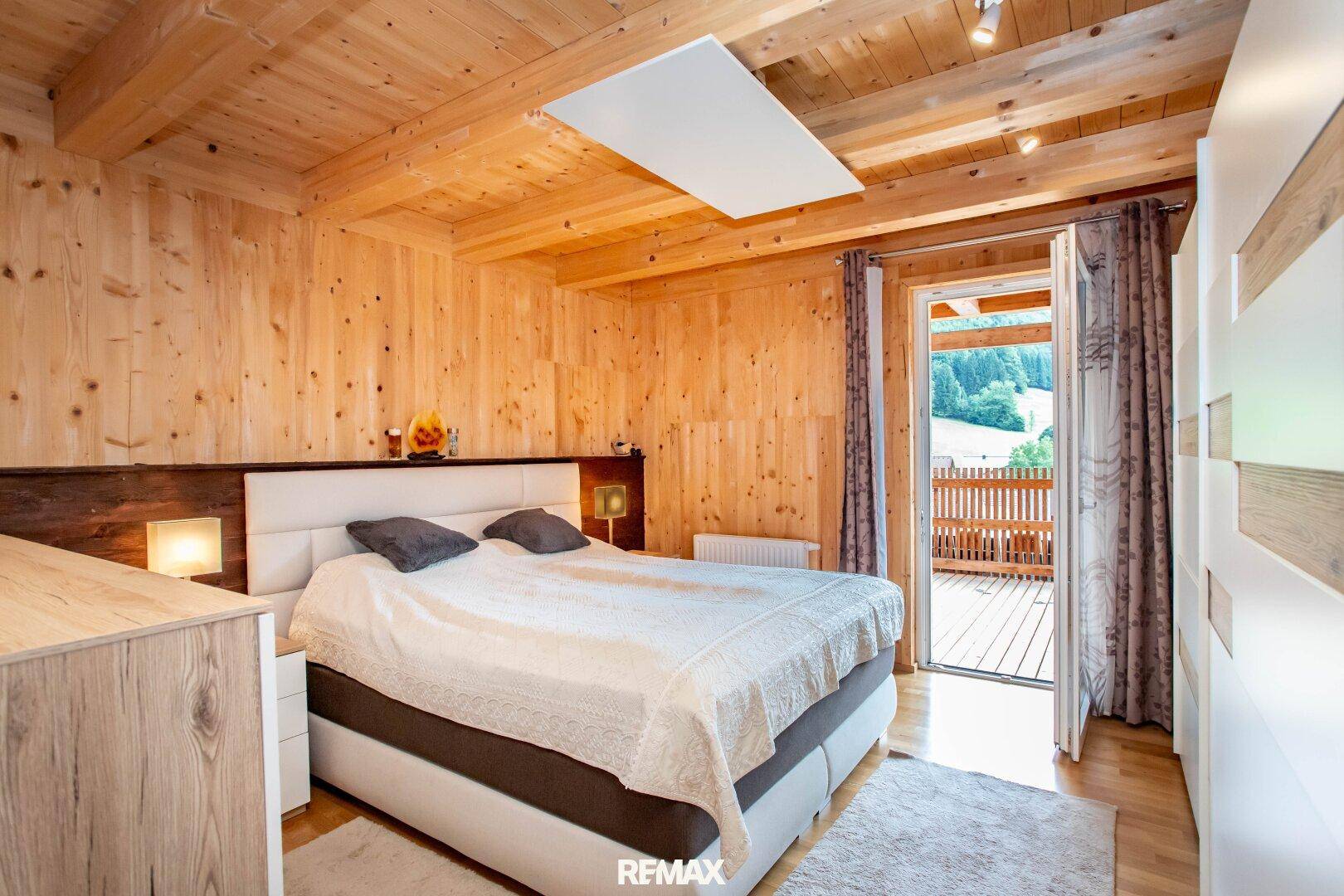 Helles Schlafzimmer mit Doppelbett, Holzvertäfelung und direktem Zugang zu einem Balkon mit Bergblick.