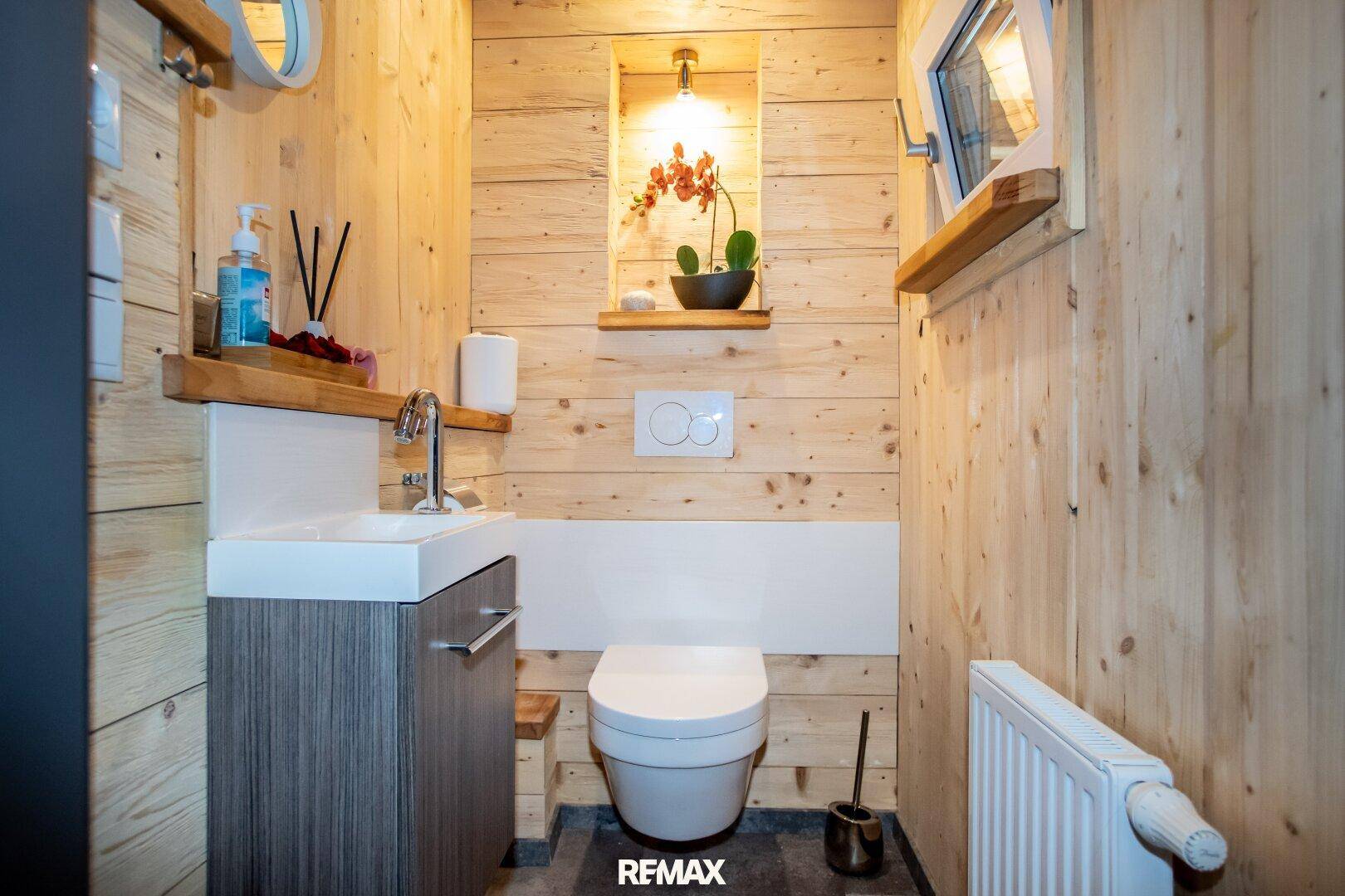 Separates WC mit Holzvertäfelung, wandhängendem WC und kleinem Handwaschbecken.