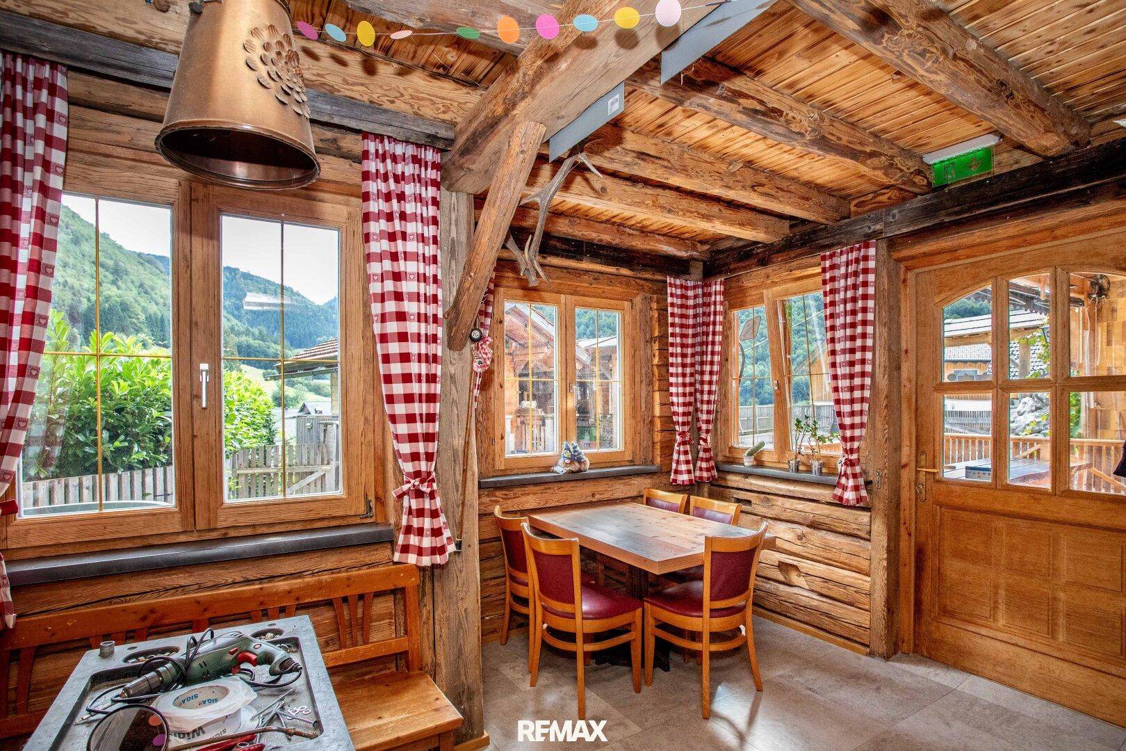 Rustikaler Essbereich mit Holztisch, Stühlen und traditionellen karierten Vorhängen.