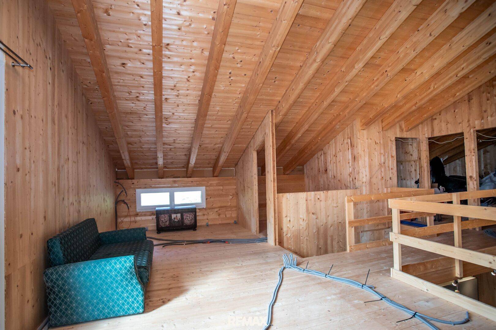 Geräumiger Dachbodenraum mit Holzverkleidung und sichtbaren Holzbalken, noch im Ausbauzustand.