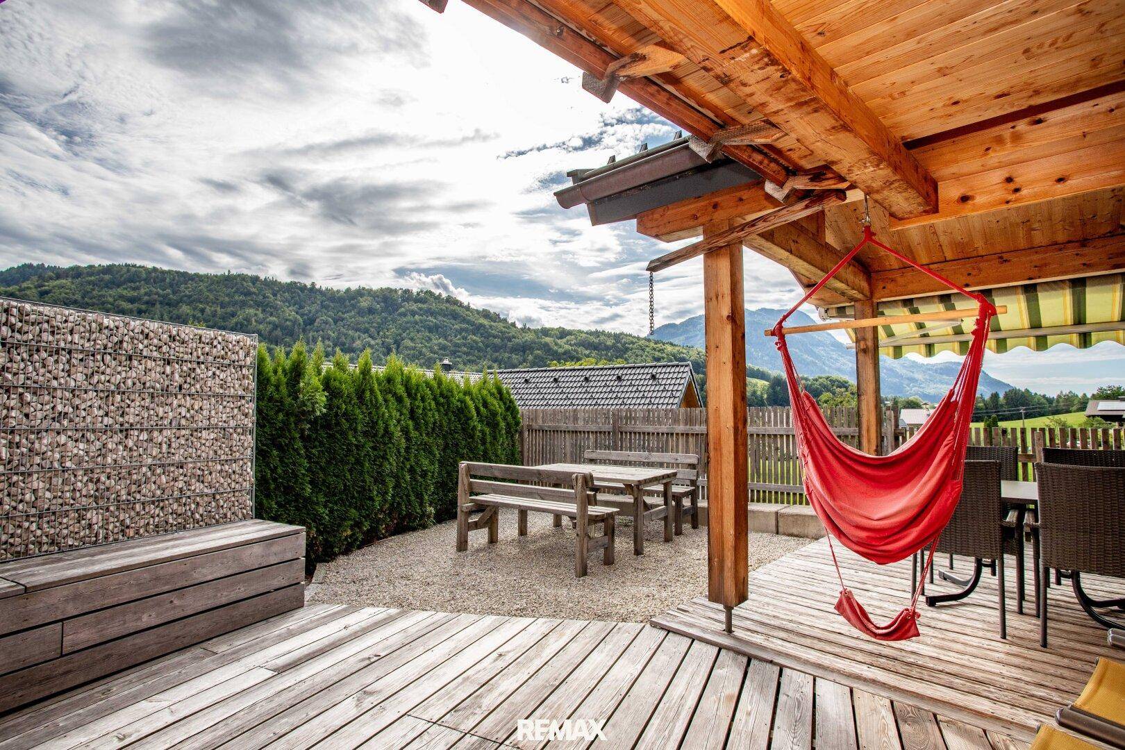 Gemütliche Terrasse mit Hängesessel, Holzbänken und Blick auf die umliegende Berglandschaft.