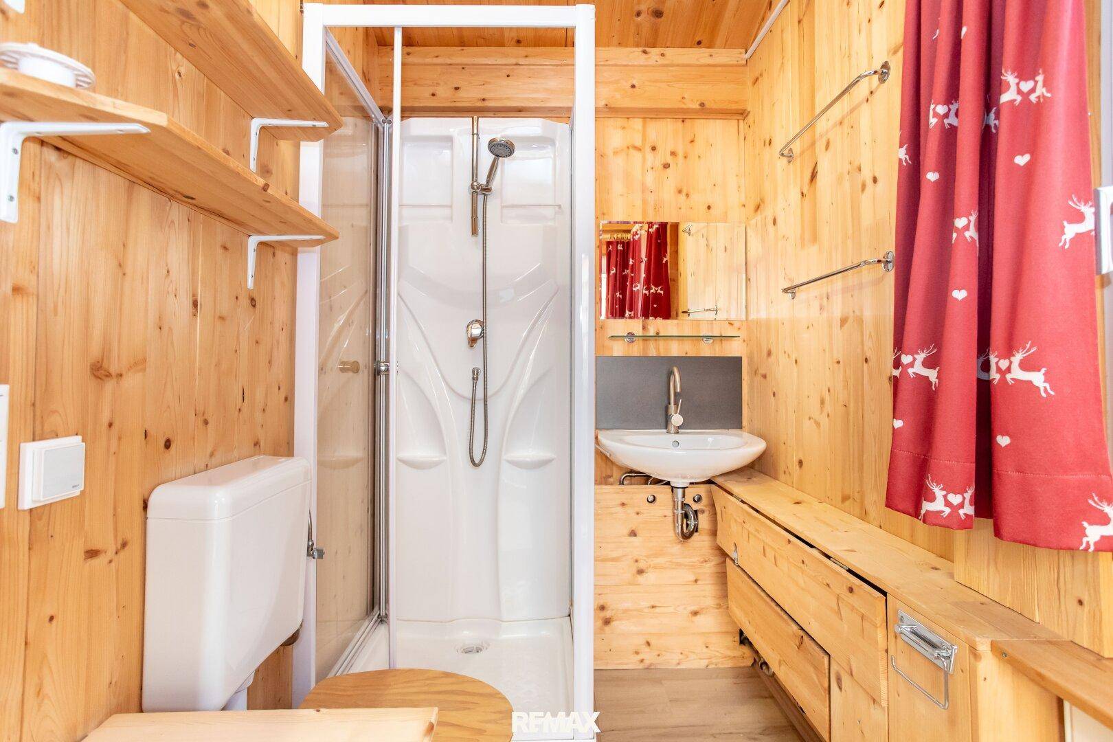 Kleines Badezimmer mit Duschkabine, Waschbecken und WC, komplett in Holz verkleidet.