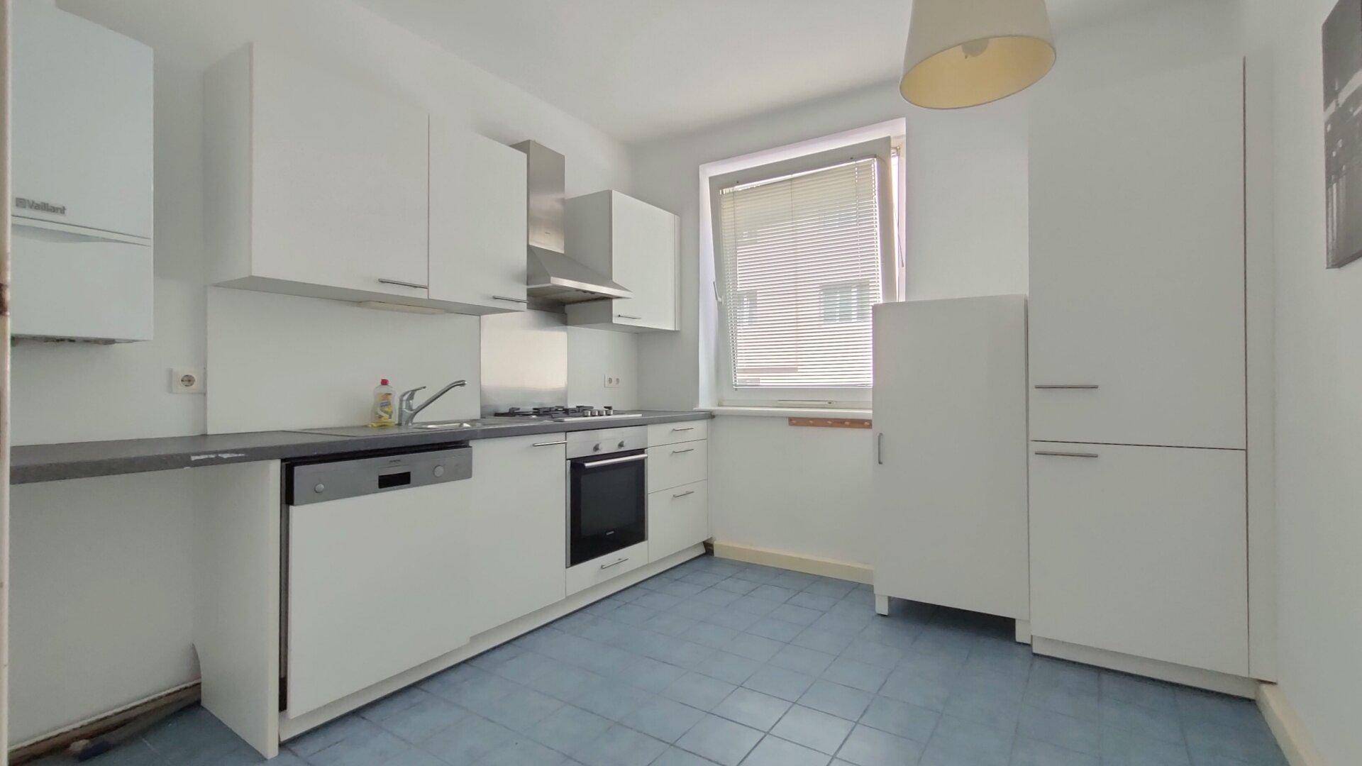 Funktionale Küche mit weißen Schränken, blauen Fliesen und integrierten Geräten wie Geschirrspüler und Backofen.