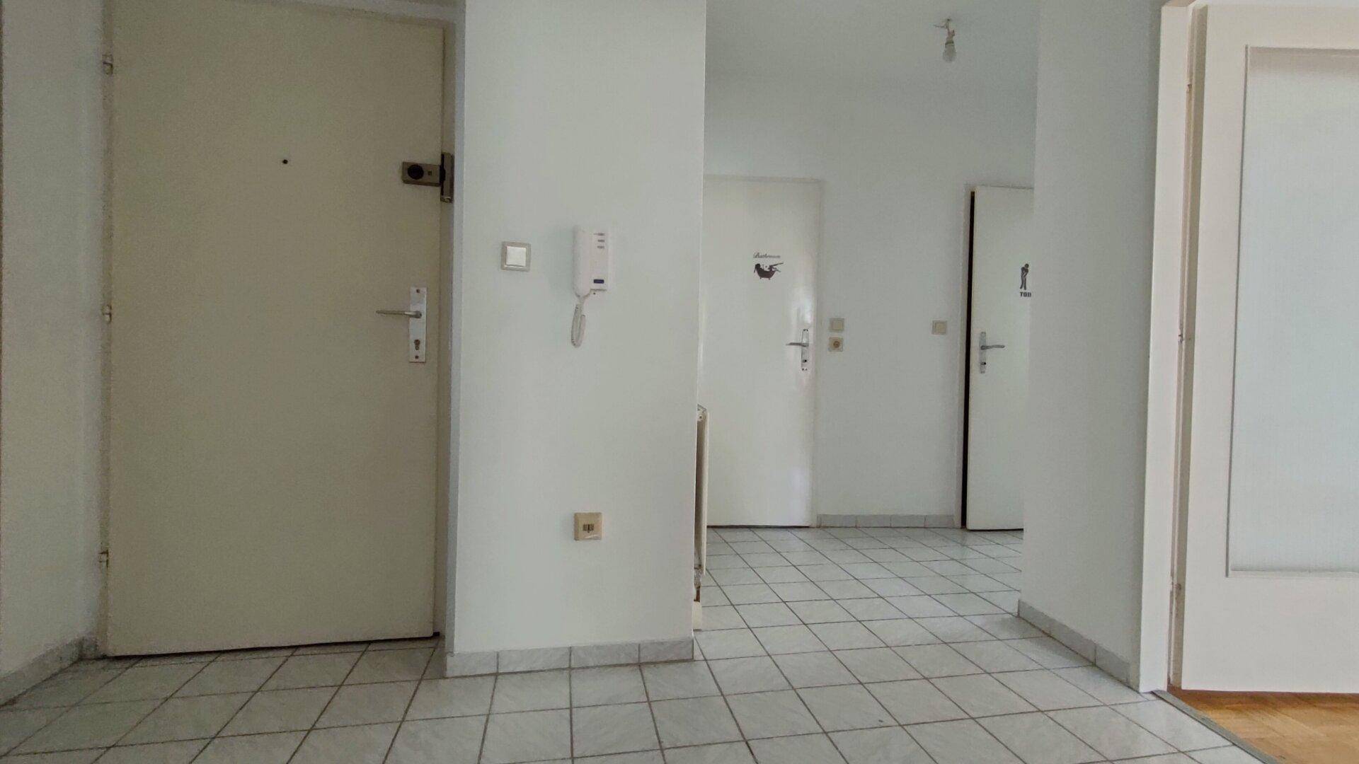 Heller Eingangsbereich mit Fliesenboden und mehreren Türen, ausgestattet mit einer Gegensprechanlage.