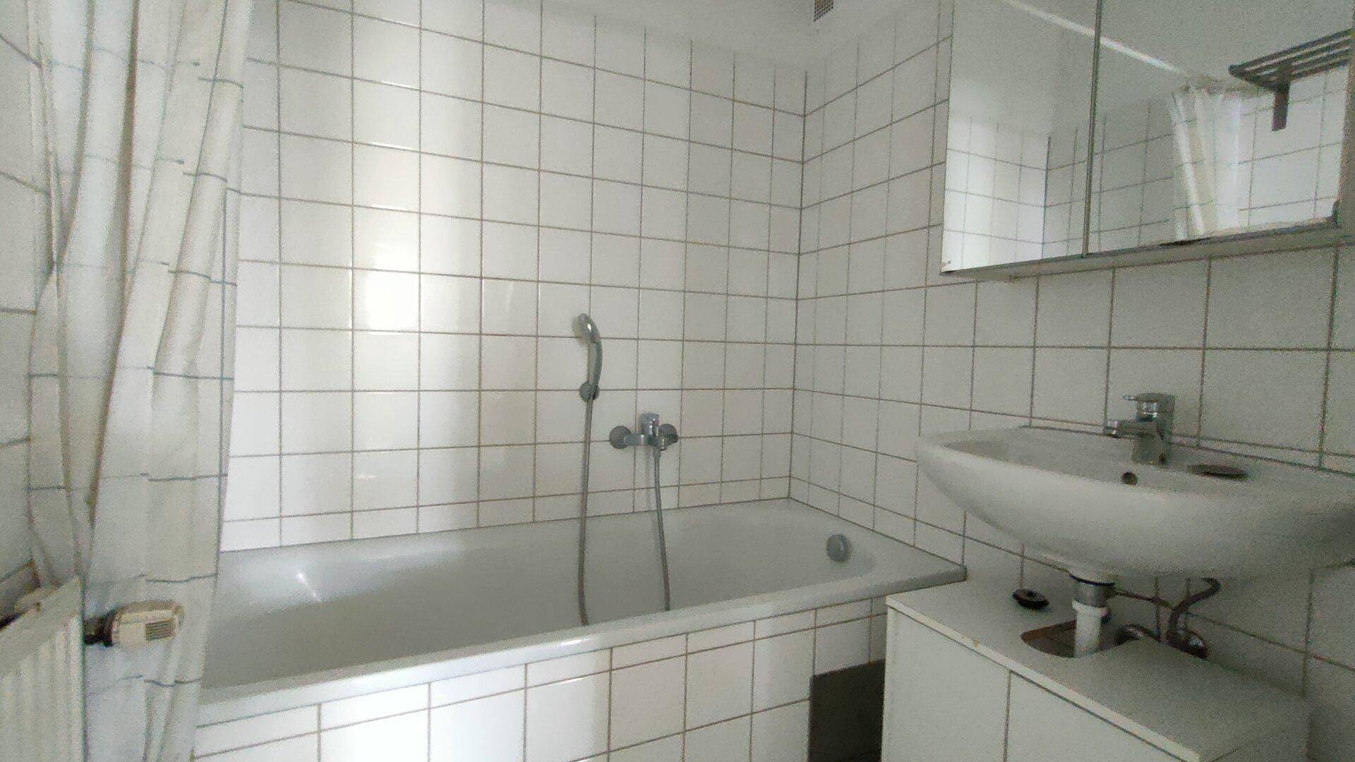 Klassisches Badezimmer mit weißen Wandfliesen, Badewanne mit Duschfunktion und einem Waschbecken mit Spiegelschrank.