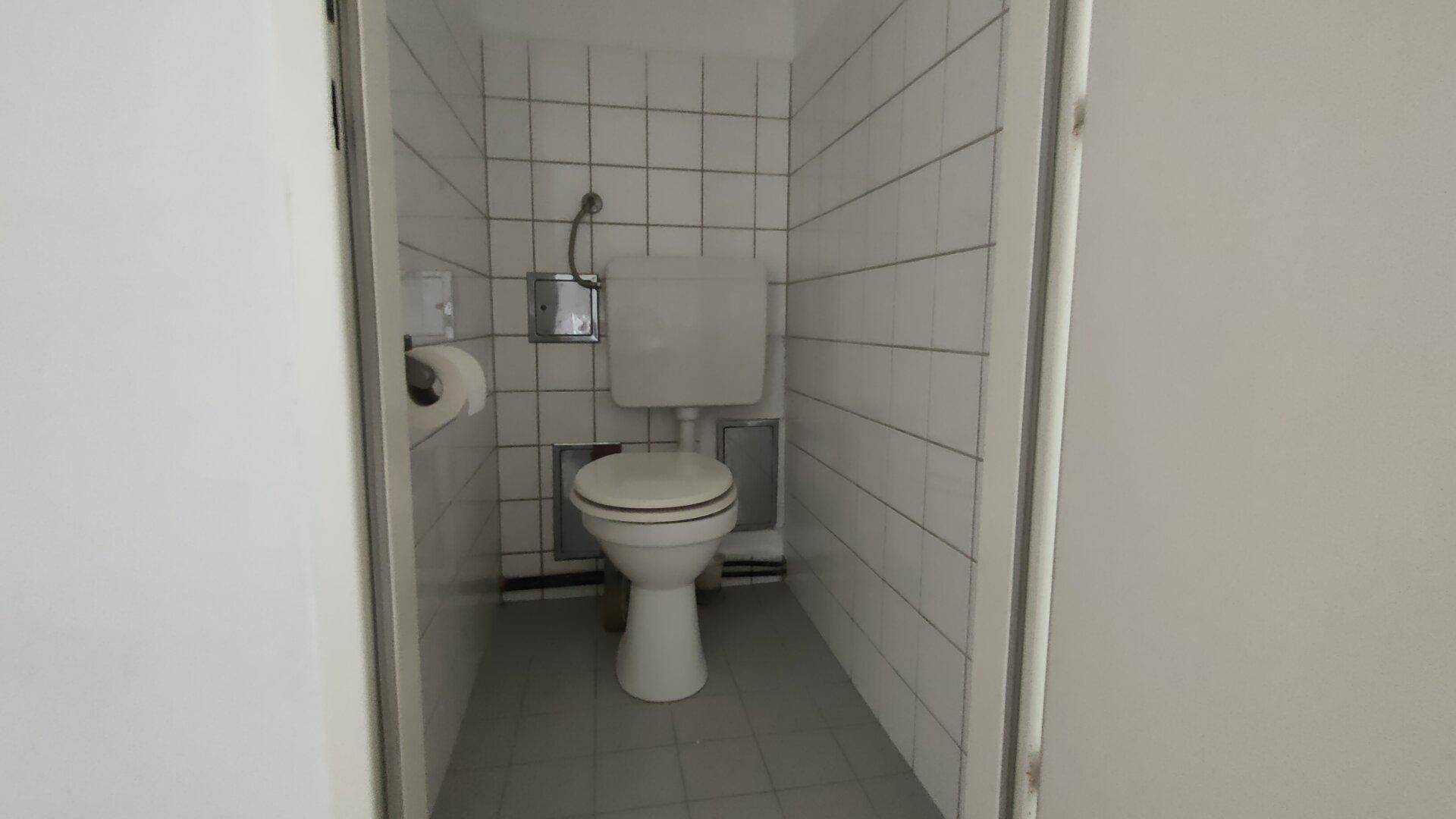 Separates WC mit weißen Fliesen, einer Toilette und einem kleinen Fenster für Belüftung.
