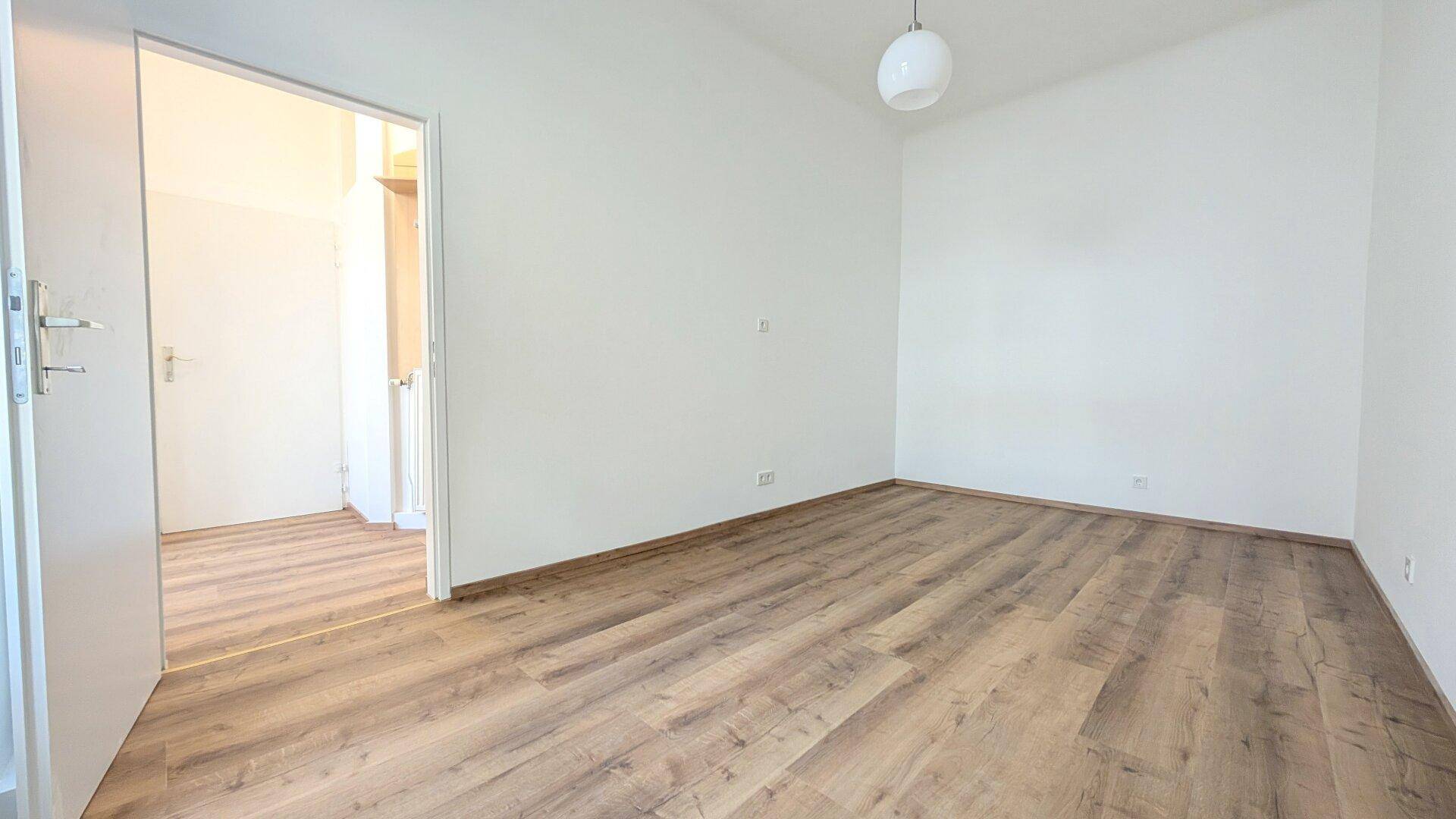 Geräumiges, helles Zimmer mit Laminatboden und weiß gestrichenen Wänden, bereit zur Einrichtung.