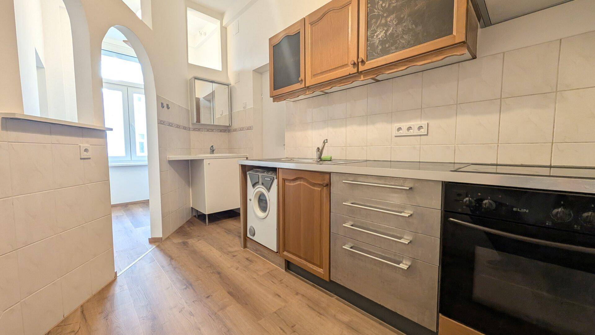 Funktionale Küche mit älteren Holzschränken, Fliesenrückwand und integrierter Waschmaschine.