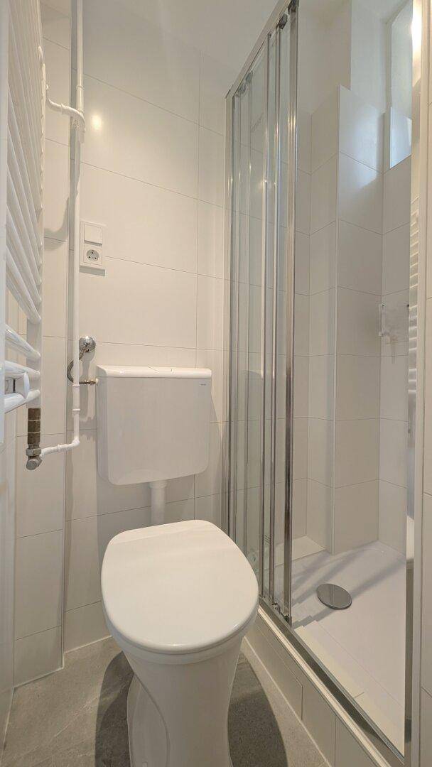 Modernes Badezimmer mit Duschkabine, WC und weiß gefliesten Wänden.
