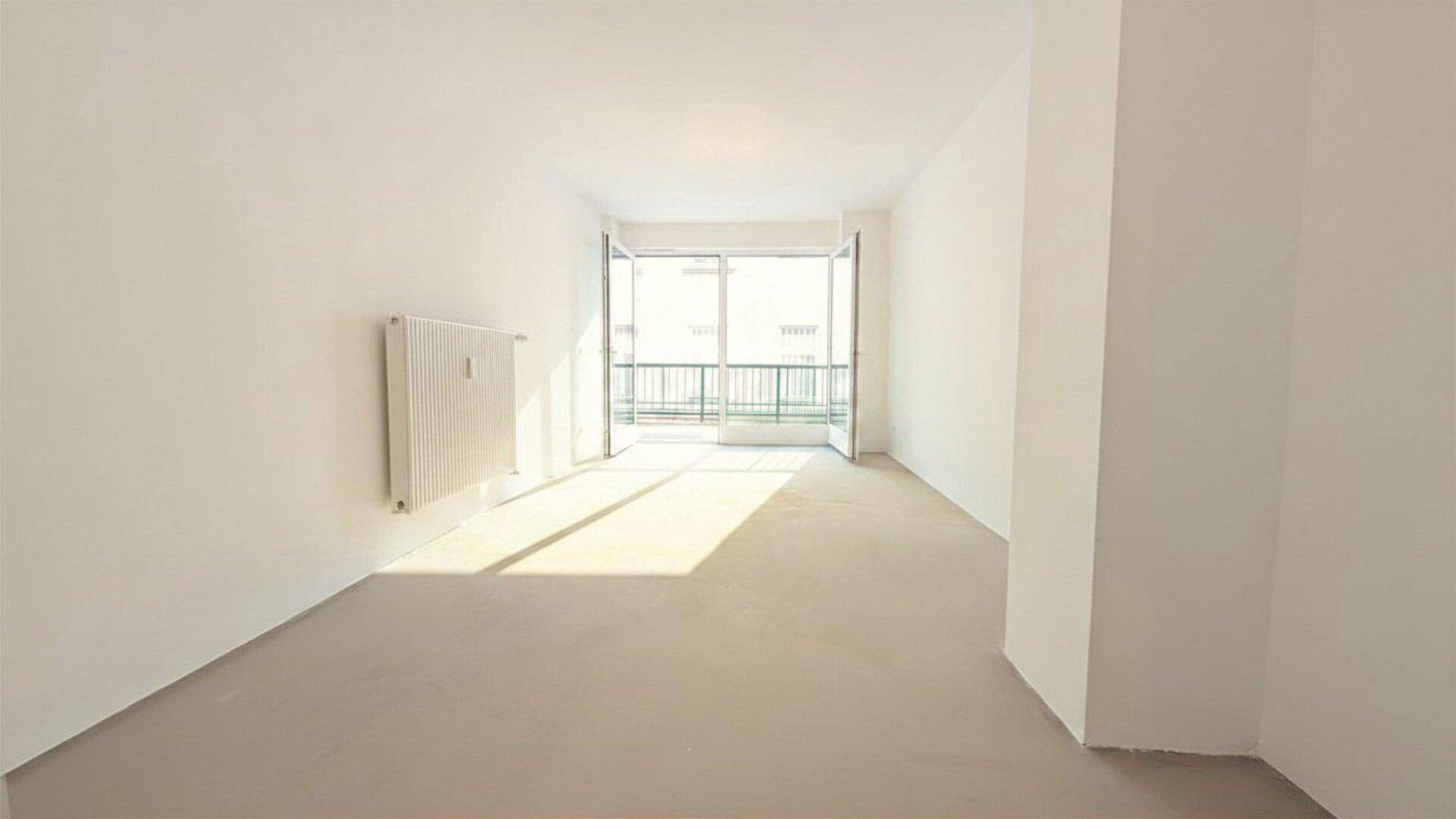 Heller, leerer Raum mit weißen Wänden, Heizkörper und Zugang zu einem Balkon mit Metallgeländer.