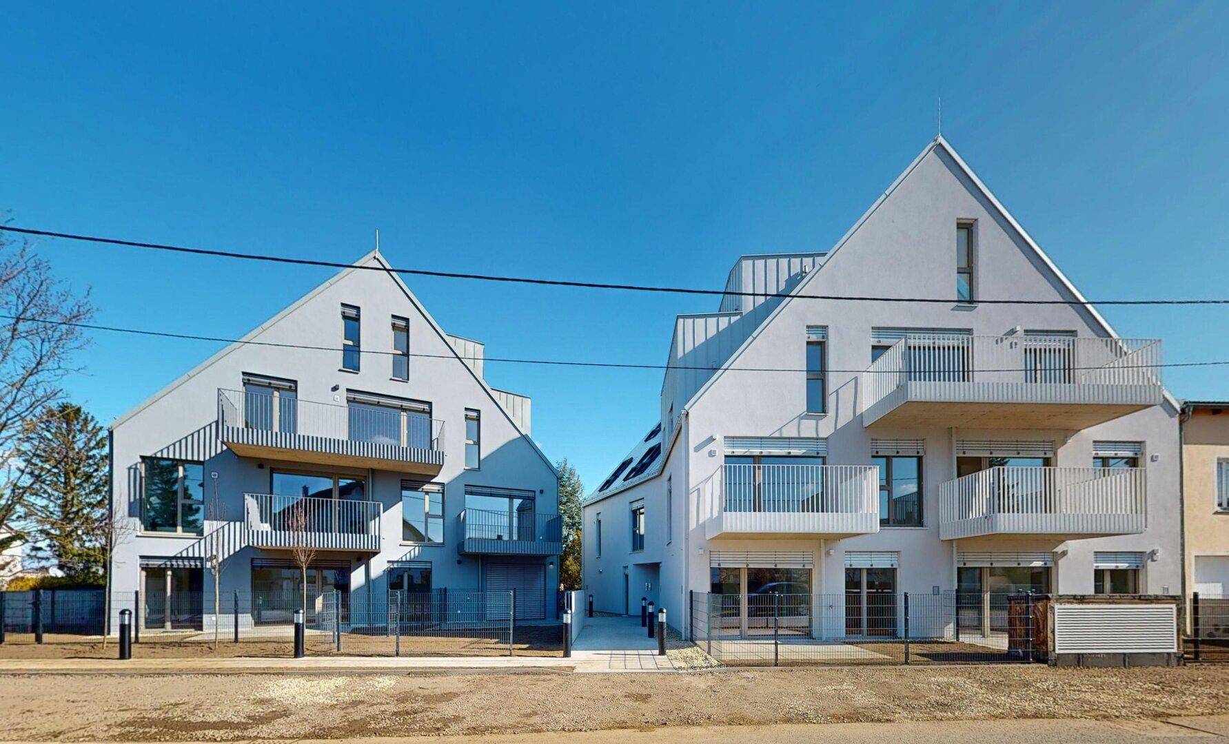 Moderne Wohngebäude mit Balkonen und Satteldächern unter blauem Himmel.