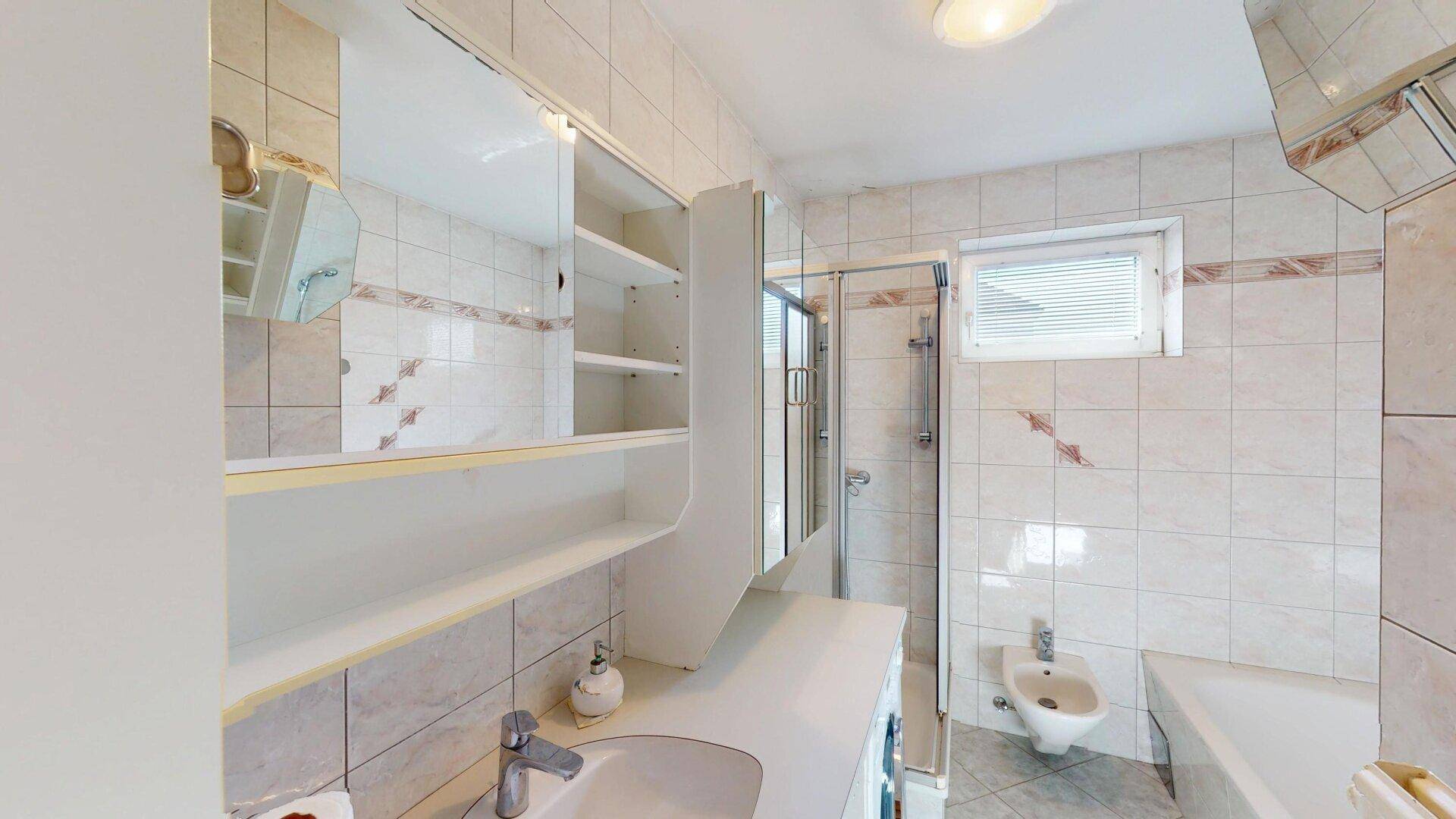 Helles Badezimmer mit Fliesen, Dusche, Badewanne, Bidet und Fenster.