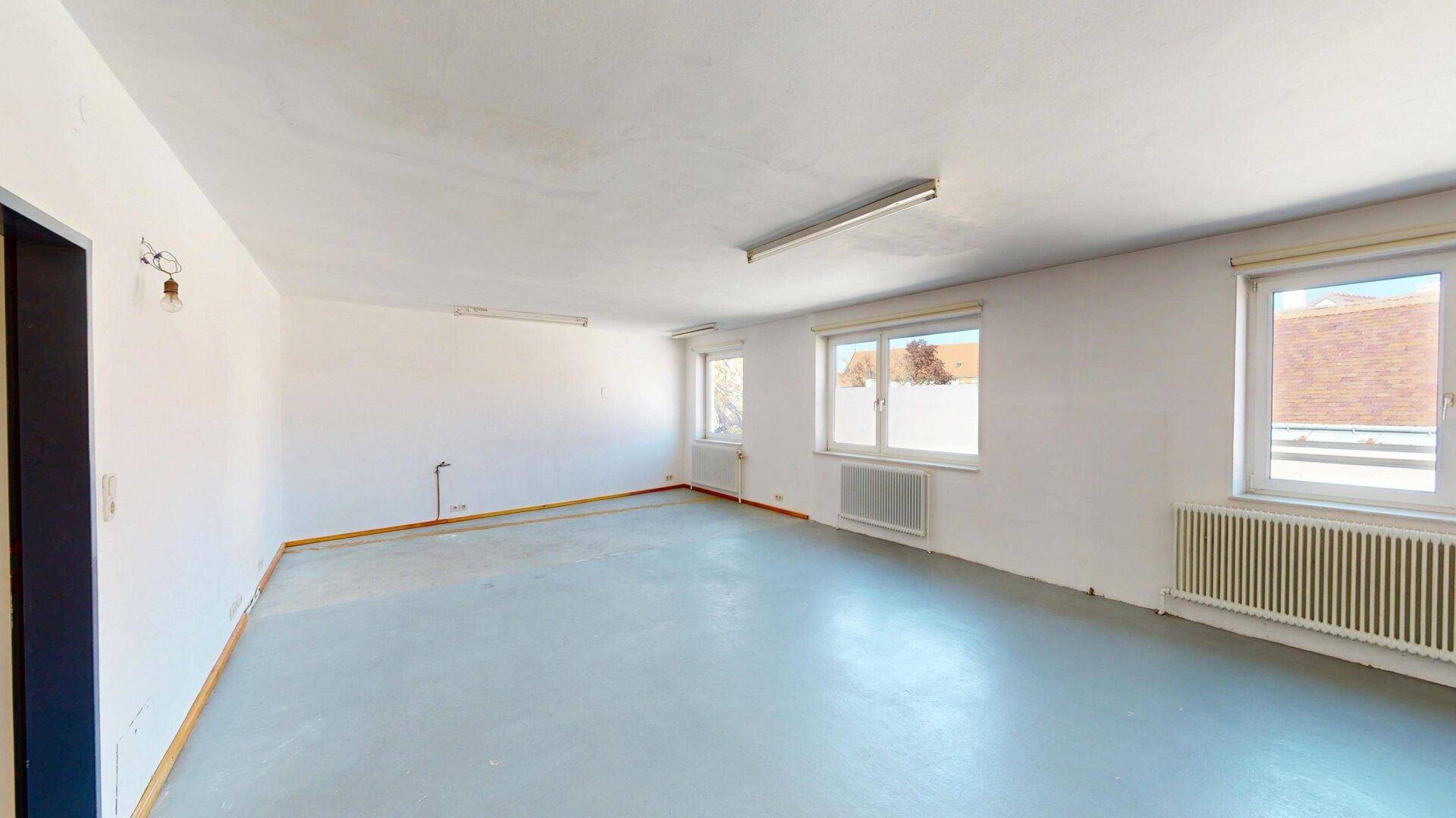 Großer, leerer Raum mit hellgrauem Boden und mehreren Fenstern, ideal als Büro.