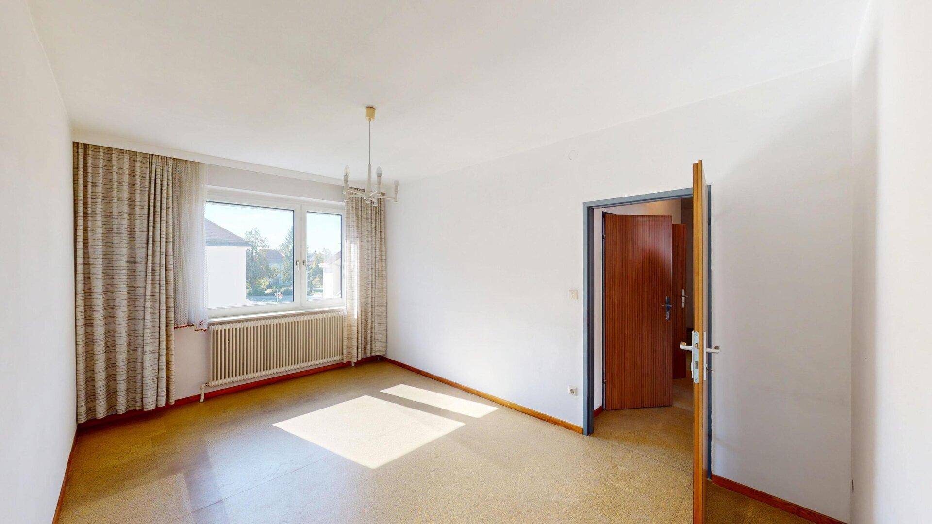 Leerer Raum mit hellem Boden, großem Fenster und Heizkörper unter dem Fenster.