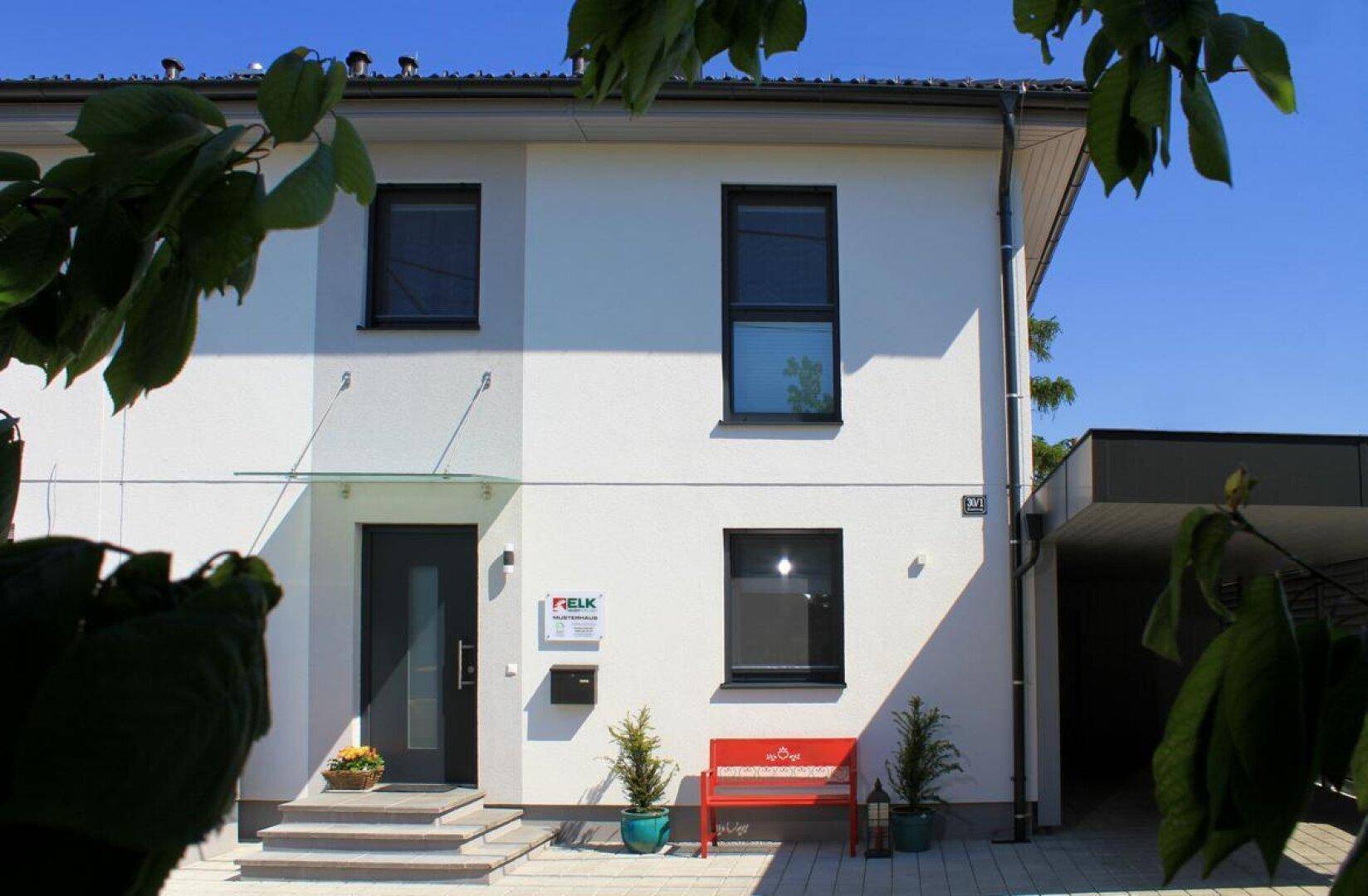 Moderne Hausfassade mit Eingangsbereich, großen Fenstern und Carport.