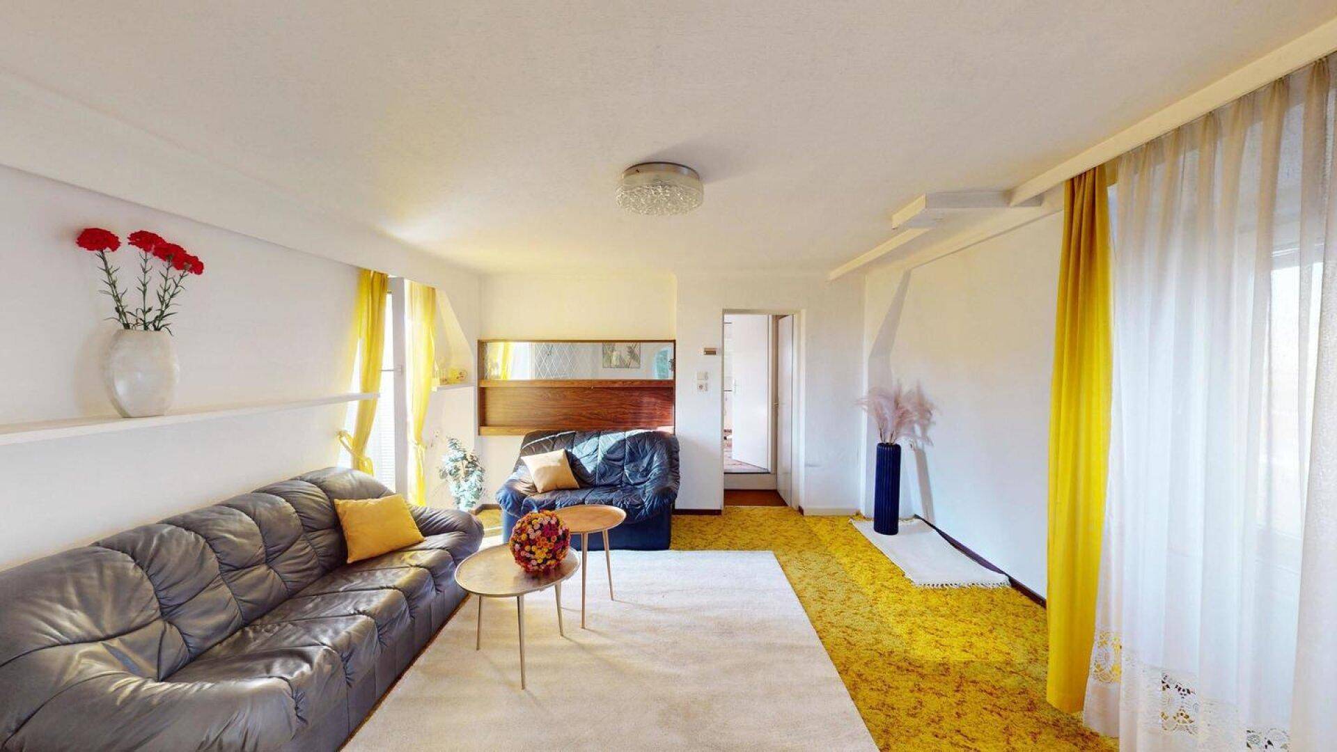 Helles Wohnzimmer mit gelbem Teppichboden, dunklen Ledersofas und gelben Vorhängen.