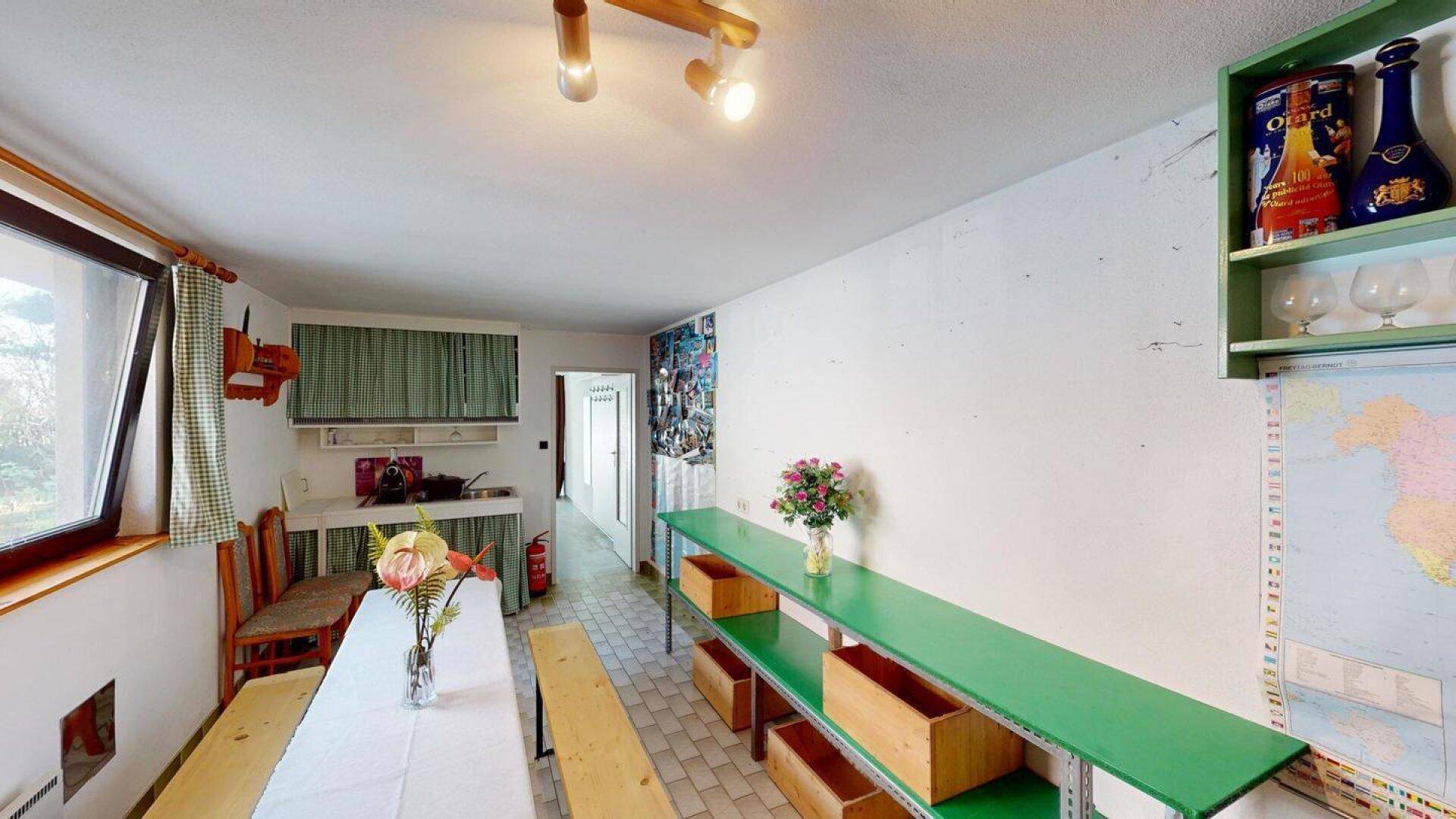 Großer Mehrzweckraum mit langer Tafel, Bänken und einer kleinen Küchenzeile.