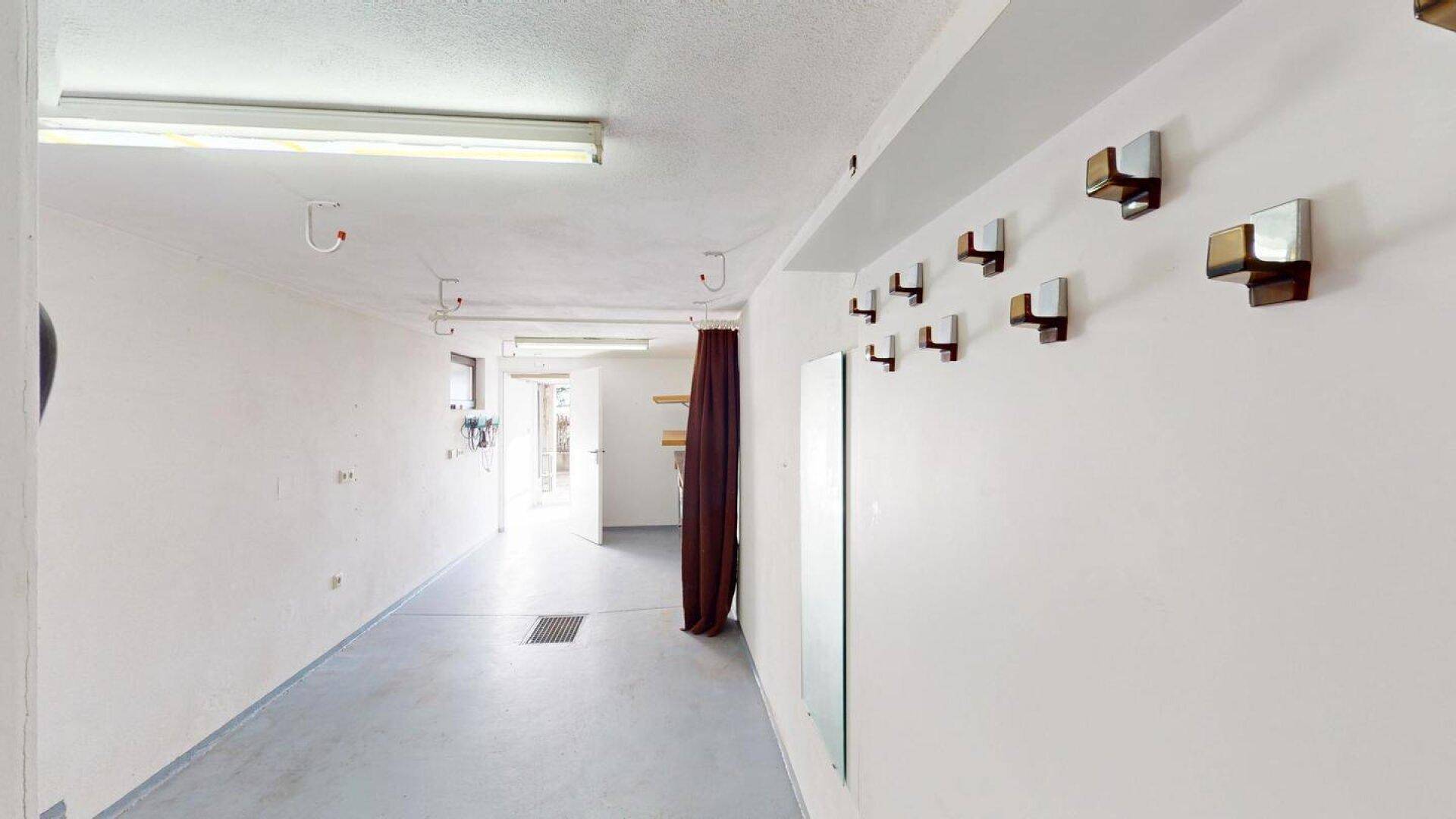 Langer, heller Flur mit weißen Wänden und einem Boden aus Beton, führt zu weiteren Räumen.