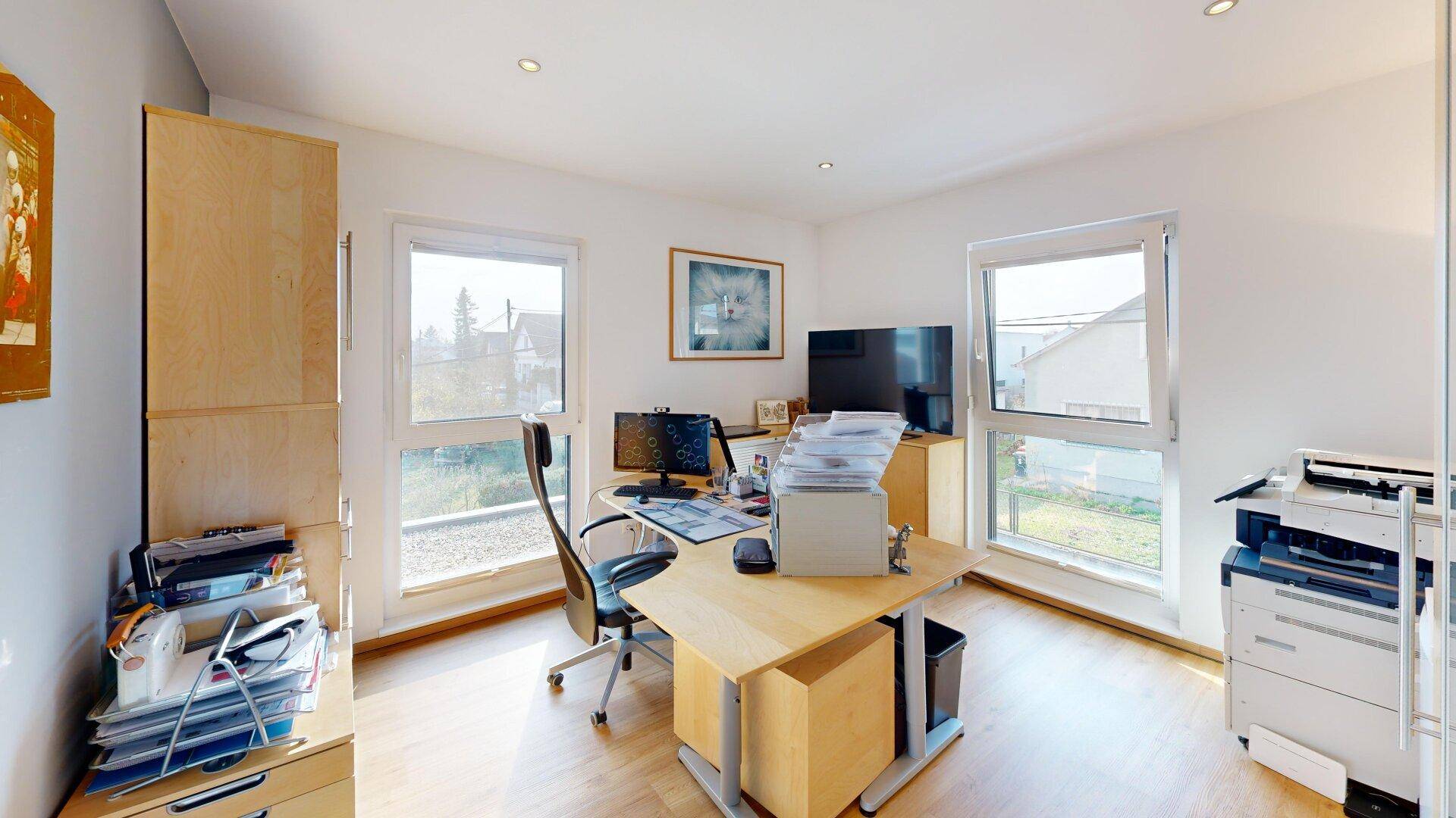 Helles Arbeitszimmer mit zwei Fenstern, Holzboden und Blick ins Freie.