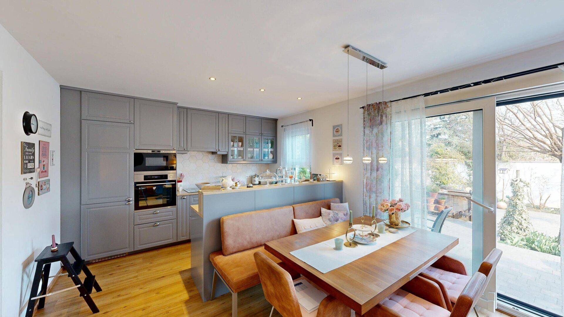 Moderne Küche mit grauen Schränken, Holztisch und direktem Zugang zur Terrasse.