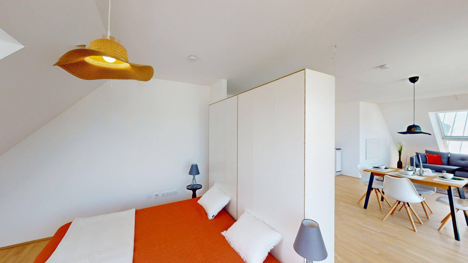 Schlafzimmer mit Holzboden und Blick in den offenen Wohnbereich sowie auf die Terrasse.