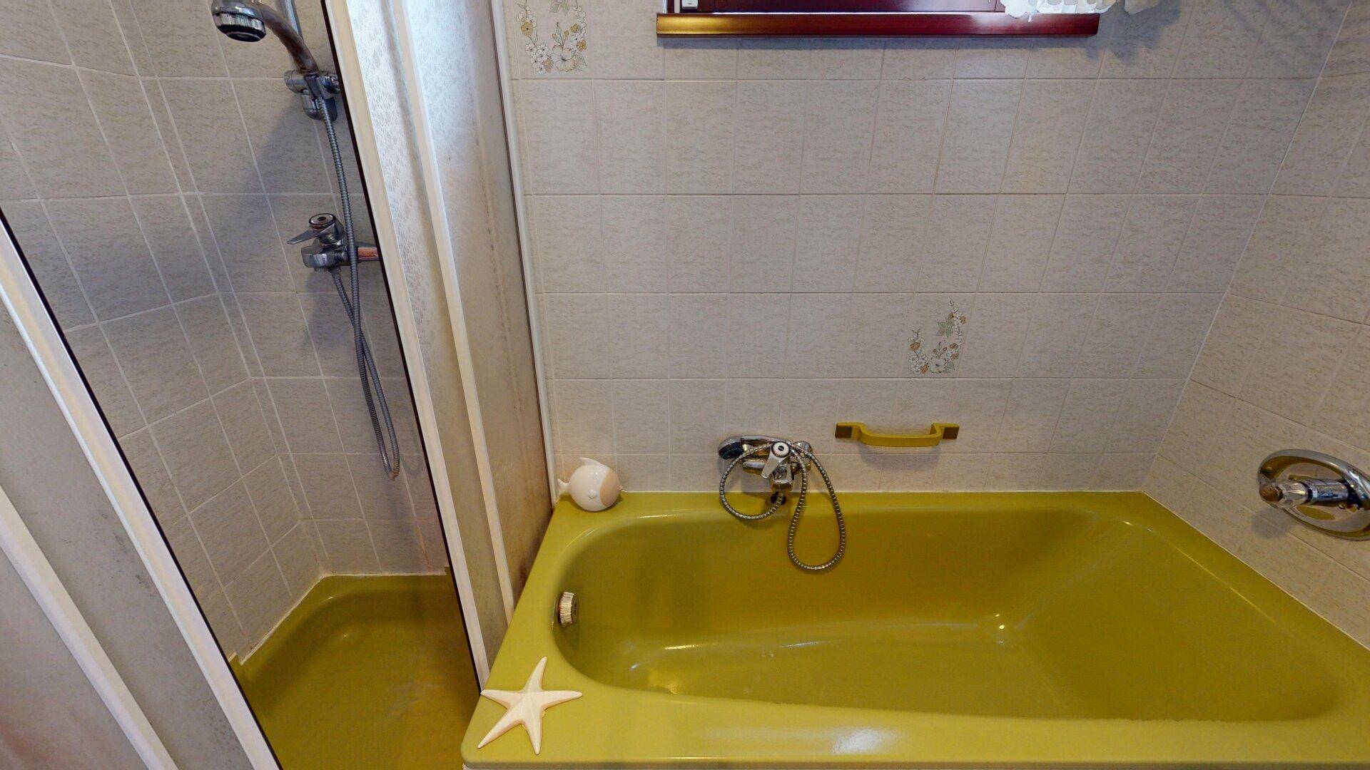Badezimmer mit gelber Badewanne, Duschbereich und hellen Fliesen im 80er-Jahre-Stil.