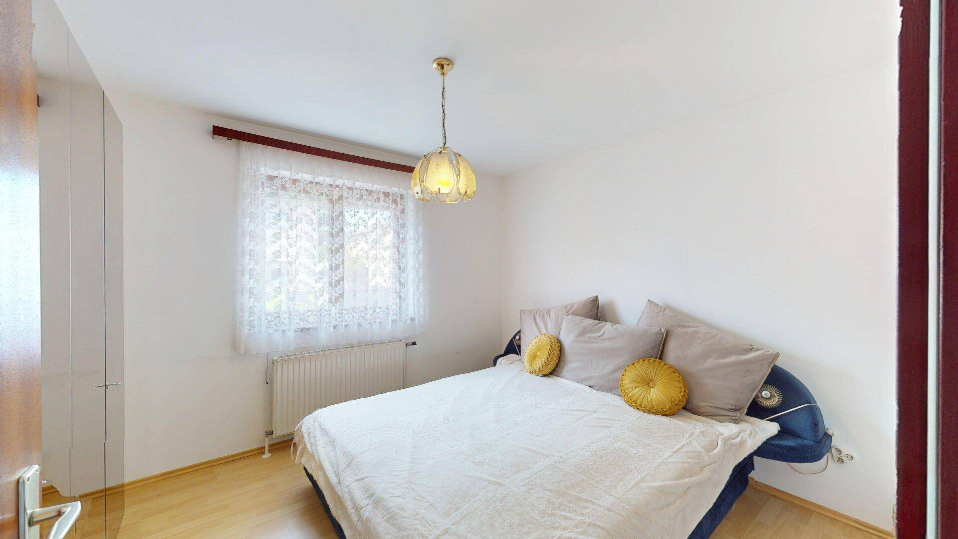 Helles Schlafzimmer mit weiß gestrichenen Wänden, Holzboden und großem Fenster.