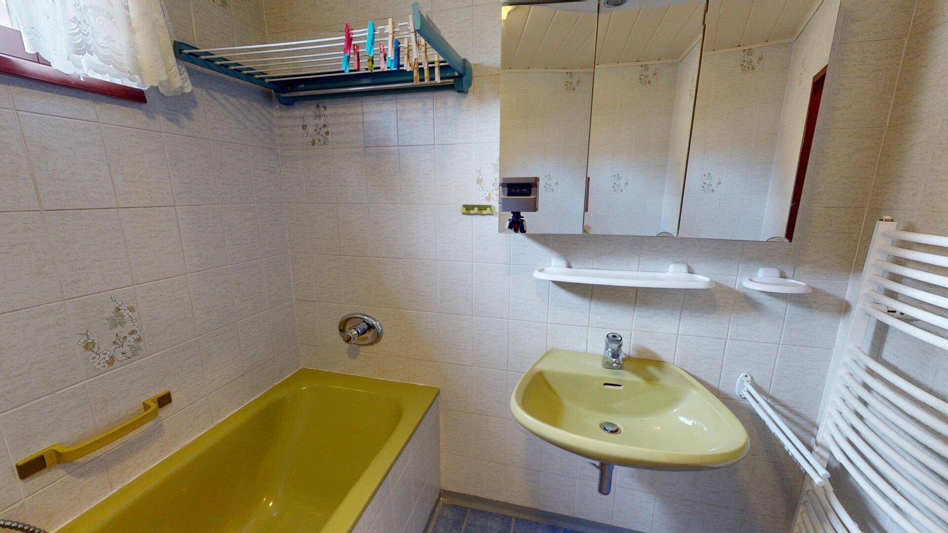 Badezimmer mit gelbem Waschbecken, Badewanne und beheiztem Handtuchhalter im Retro-Stil.