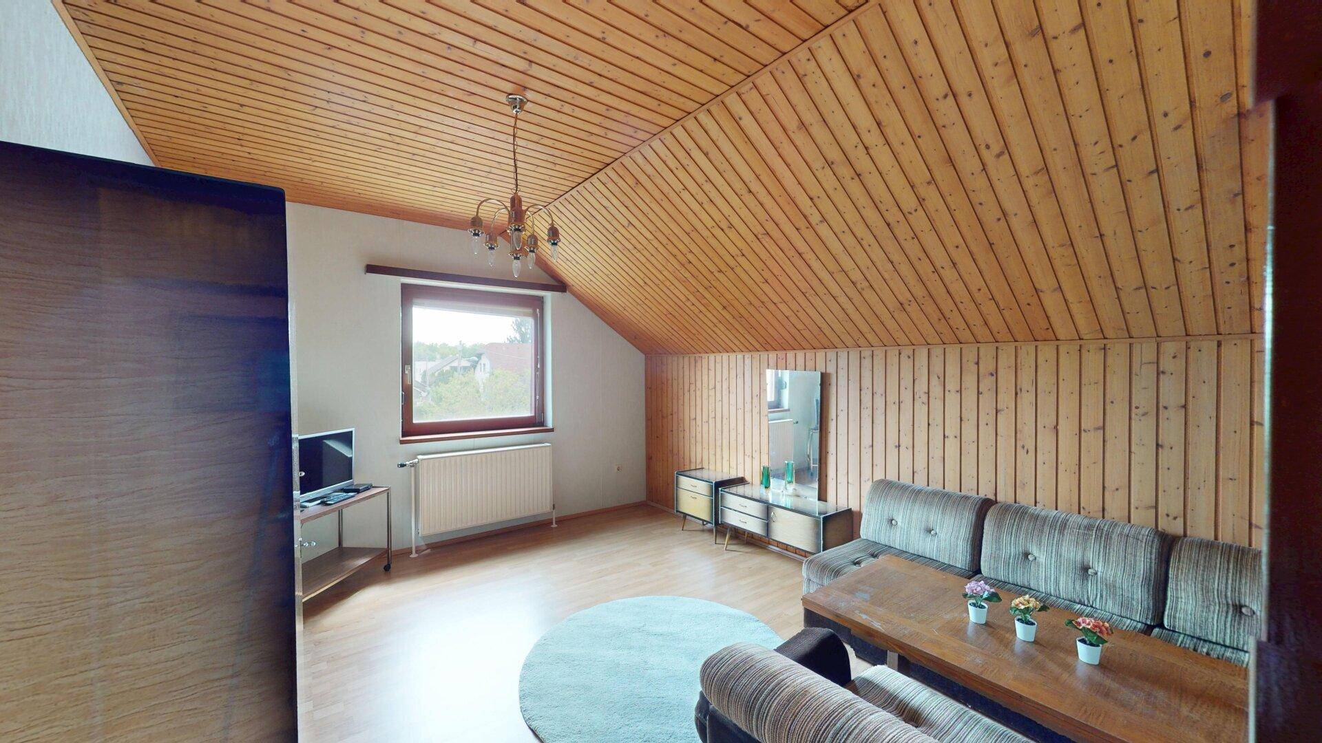Geräumiges Dachgeschoss-Wohnzimmer mit Holzdecke, Sofa und Fenster mit Ausblick.