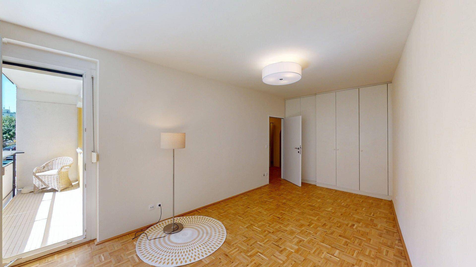Geräumiges Schlafzimmer mit Einbauschränken, Parkettboden und Balkonzugang.