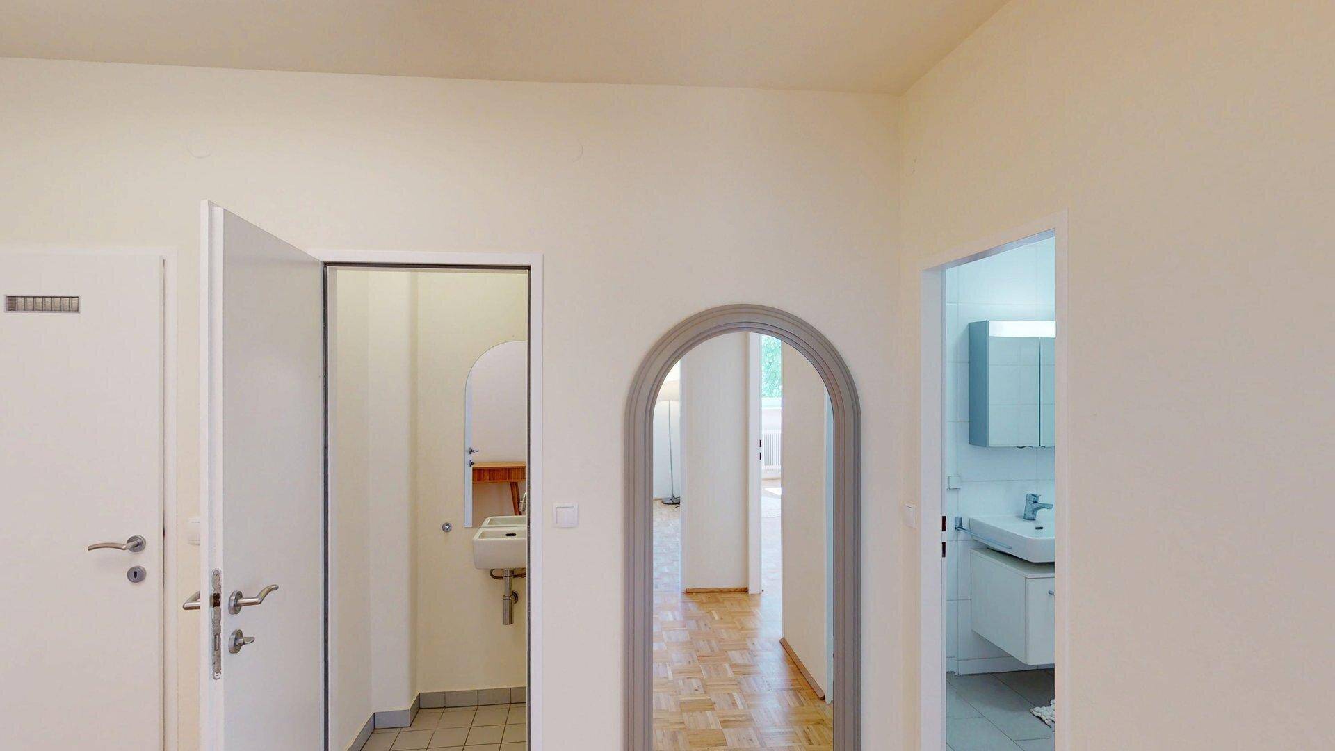 Flur mit Parkettboden und Rundbogen, der zu Badezimmer und WC führt.