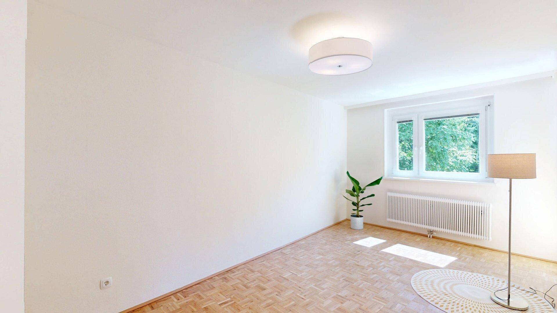 Geräumiges Zimmer mit Parkettboden und großem Fenster, das viel Tageslicht hereinlässt.
