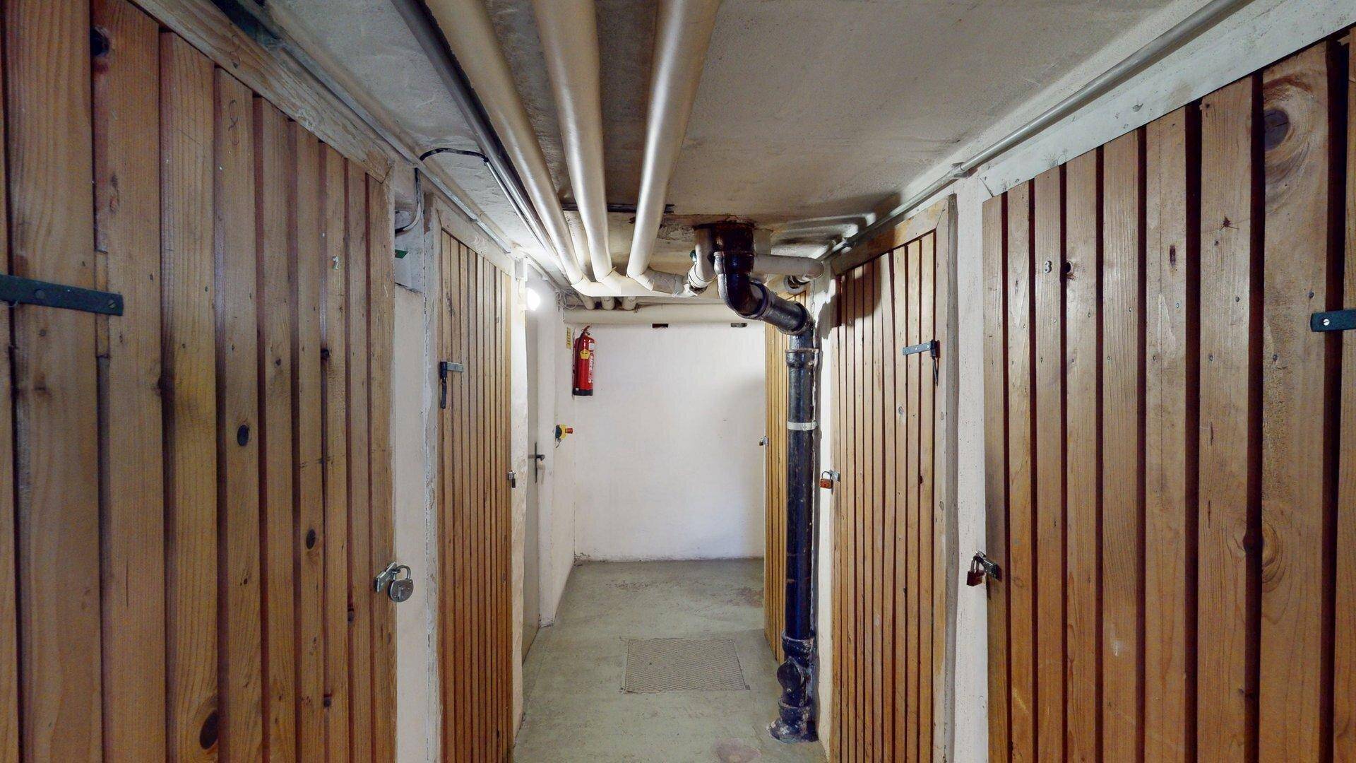 Kellerabteil mit Holzverschlägen und sichtbaren Rohren, bietet zusätzlichen Stauraum.
