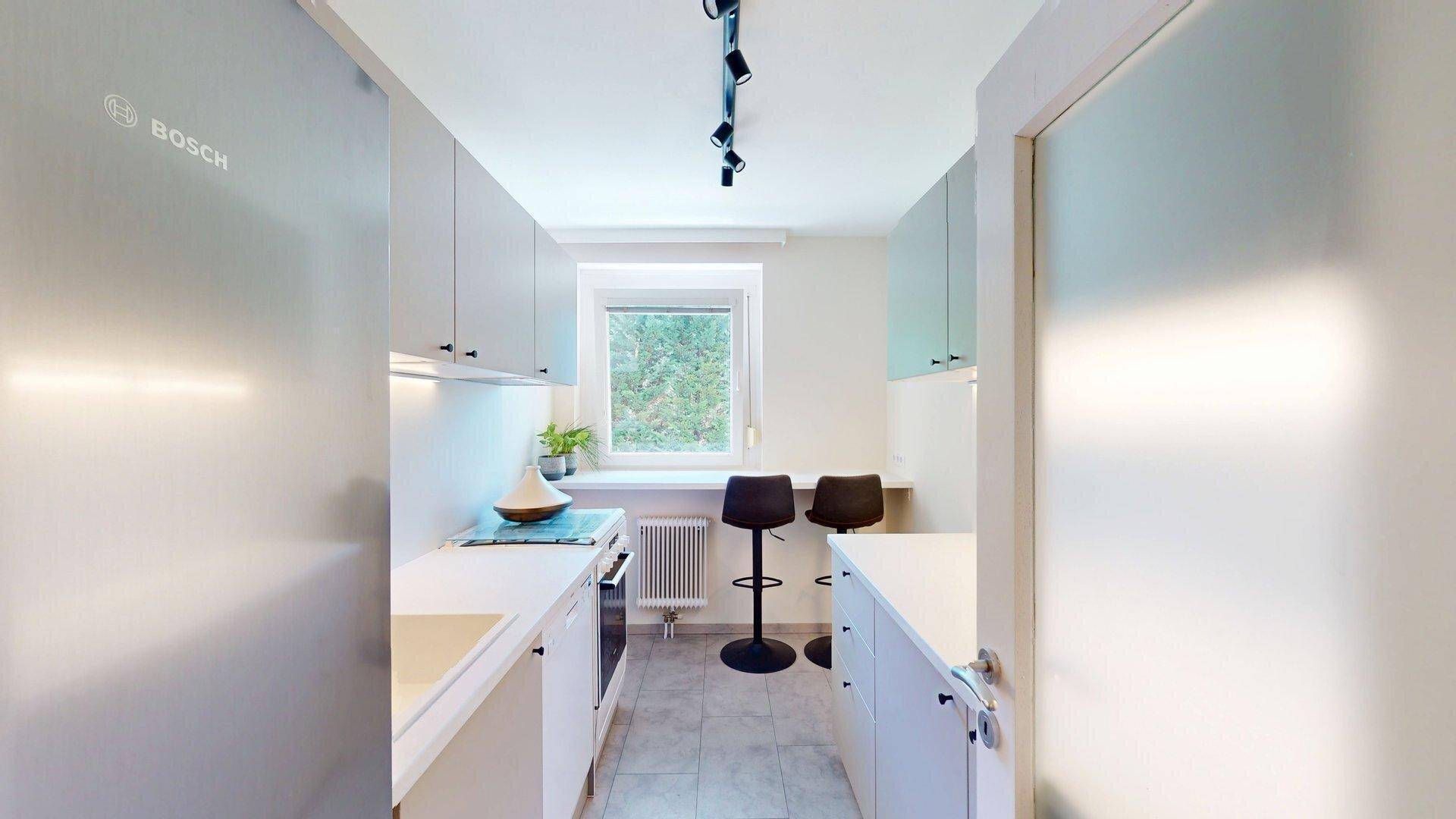 Moderne Küche mit grauen Schränken, Bosch-Kühlschrank und Essbereich am Fenster.
