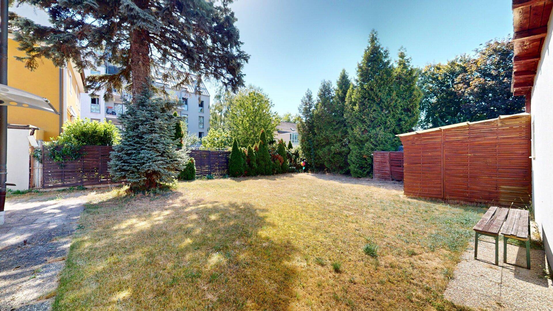Großer, sonniger Gartenbereich mit Rasenfläche, umzäunt und mit einem Gartenhaus.