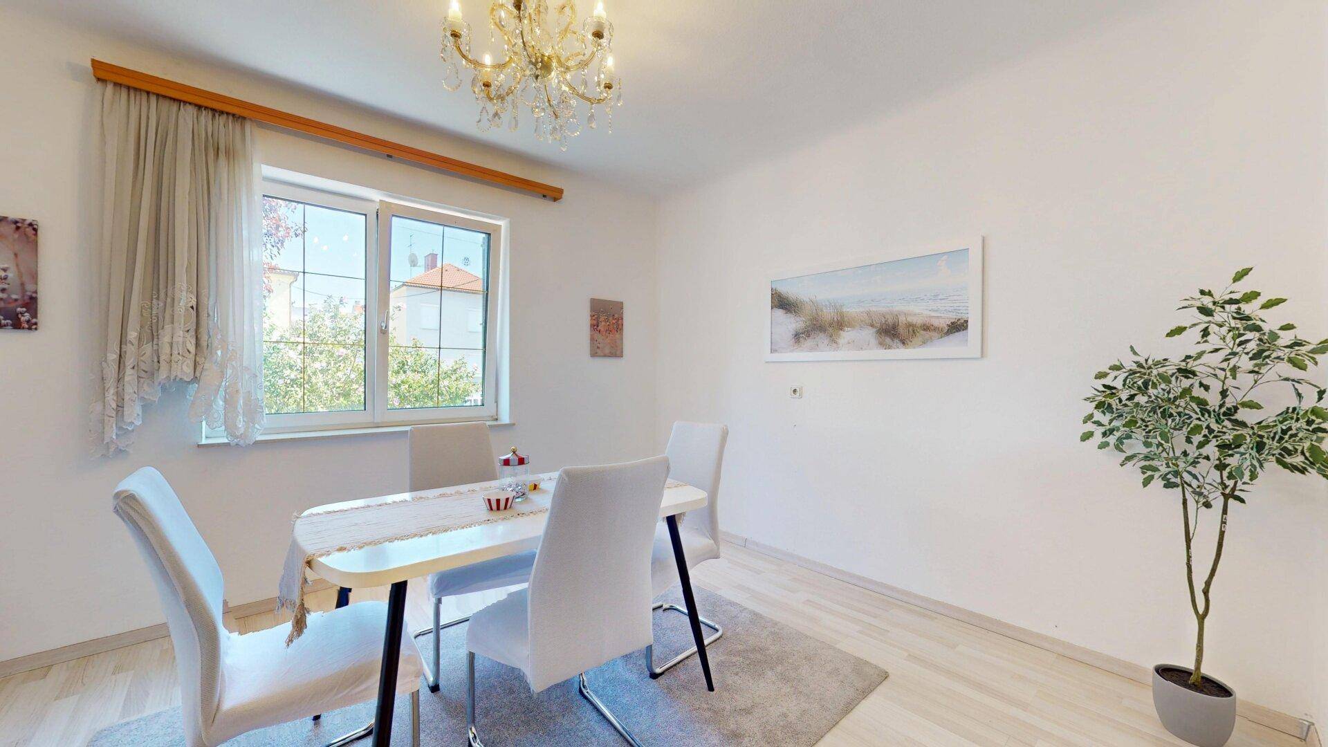 Helles Esszimmer mit modernem Esstisch, weißen Stühlen und Kronleuchter.