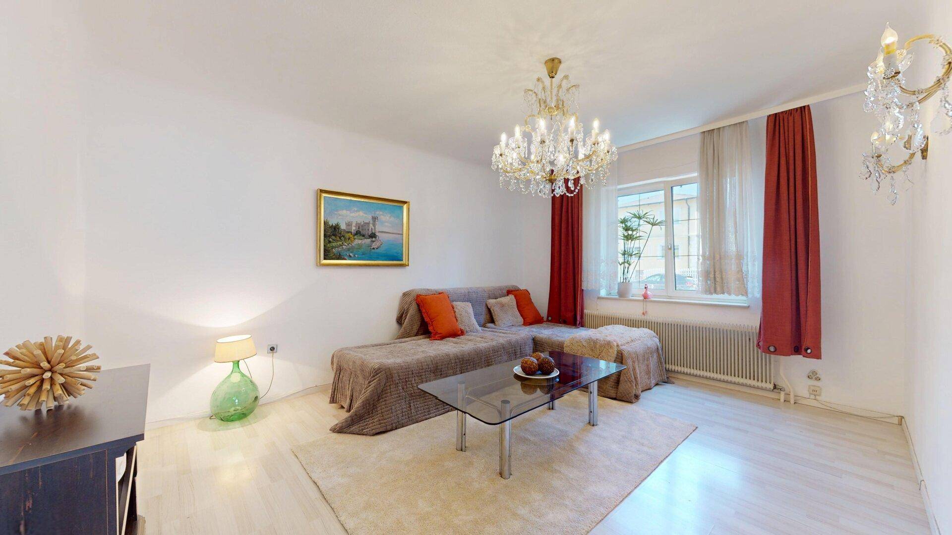 Geräumiges Wohnzimmer mit großem Sofa, Couchtisch und eleganten Kronleuchtern.