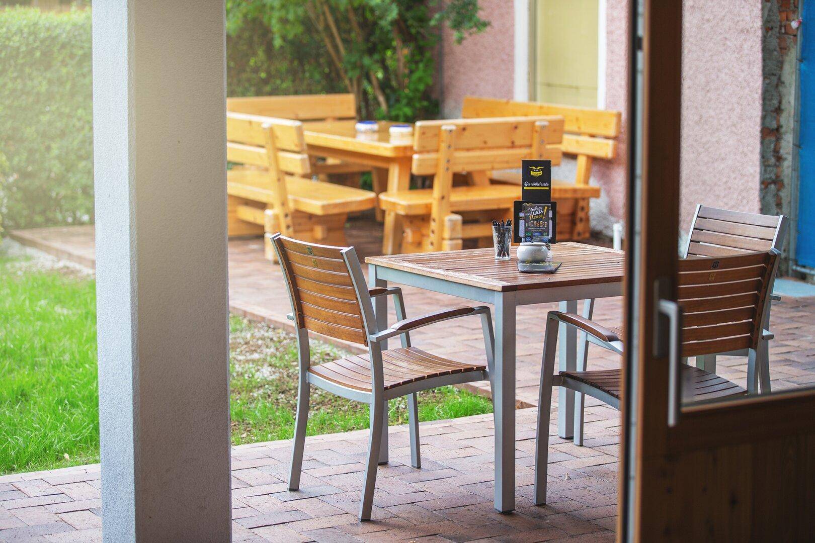 Einladender Außenbereich mit Holztischen und Bänken auf einer gepflasterten Terrasse neben Rasenflächen.