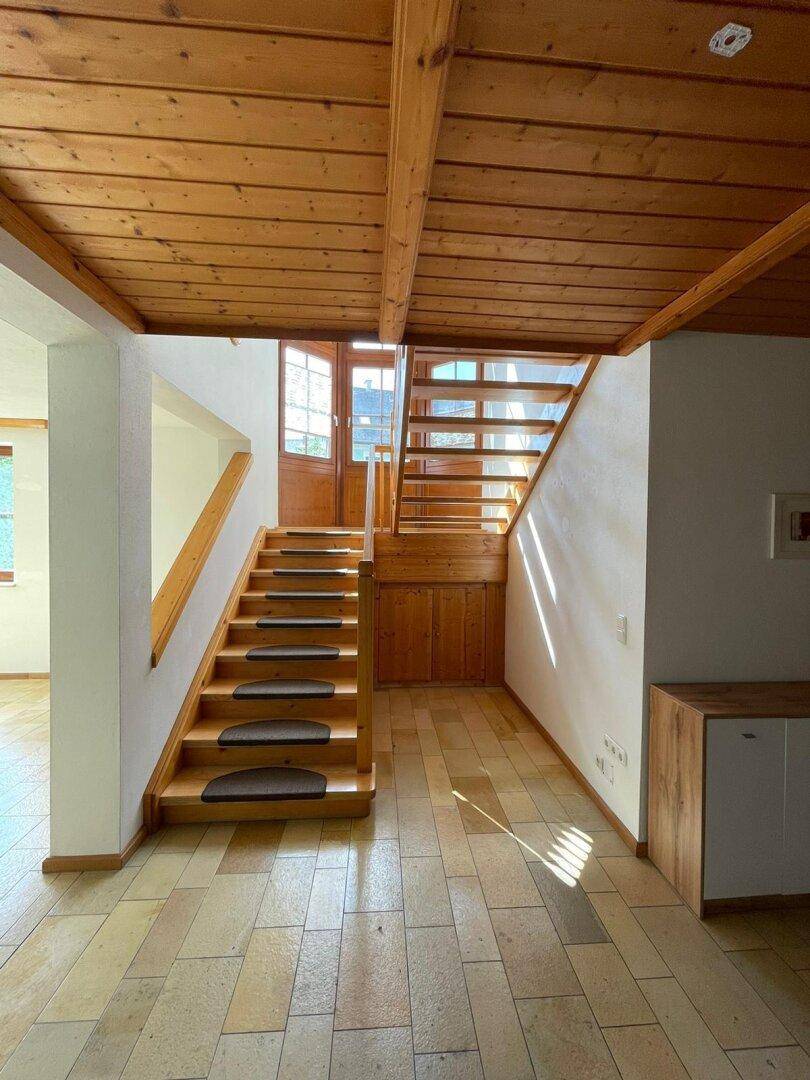 Heller Eingangsbereich mit Holztreppe, Fliesenboden und einer Holzdecke.