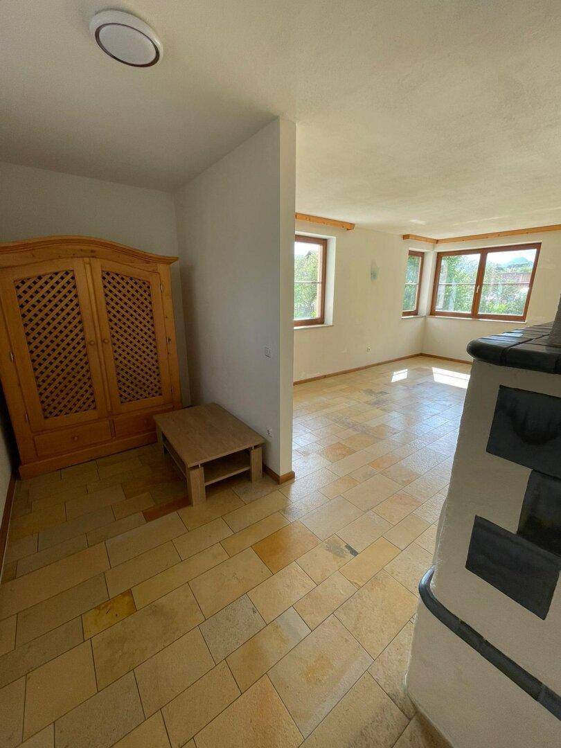 Heller, leerer Raum mit Fliesenboden, Holzschrank und mehreren Fenstern.
