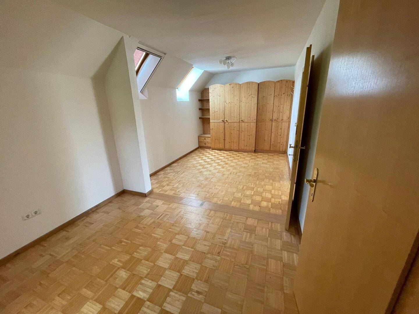 Schlafzimmer mit Parkettboden, Dachschräge, Einbauschränken und Dachfenster.