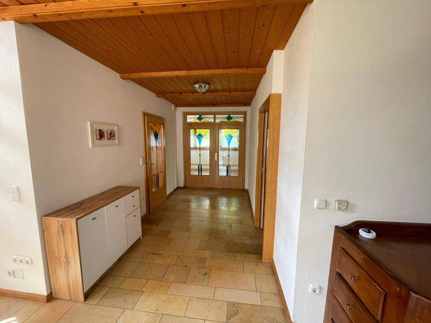 Heller Flur mit Fliesenboden, Holzdecke und einem modernen Sideboard.