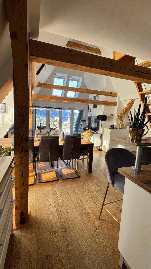 Offener Wohn- und Essbereich im Dachgeschoss mit Holzbalken und Panoramablick.