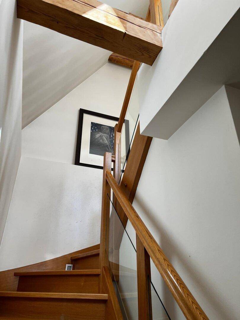 Moderne Holztreppe mit Glasgeländer und Holzbalken, die in die obere Etage führt.